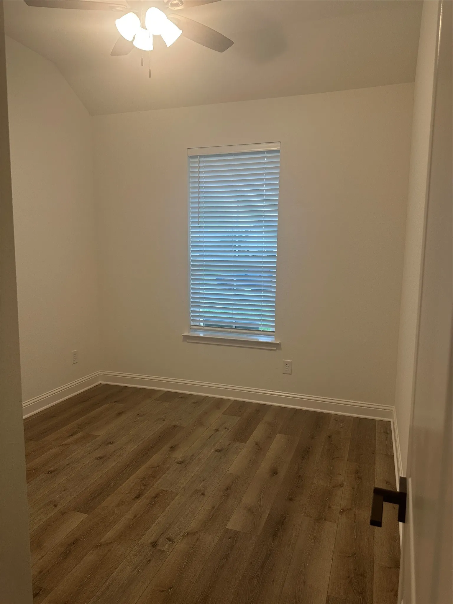 Vaulted ceiling, ceiling fan with integrated lighting, wood-finish flooring, window with blinds, and white trim