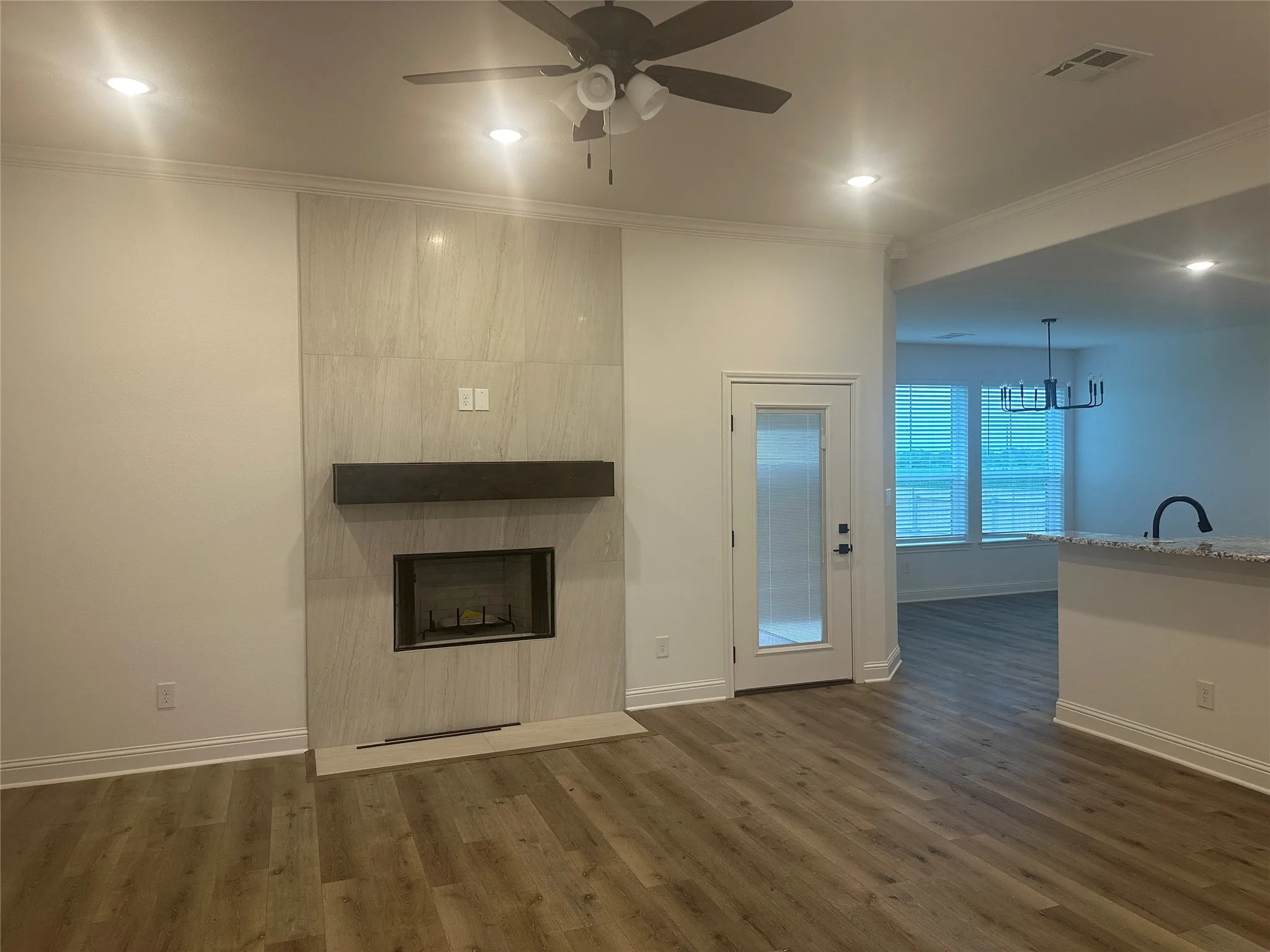 Wood-finish flooring throughout, ceiling fan with integrated lighting, recessed lighting, fireplace with a tiled surround and wood mantel, and a door with frosted glass panel
