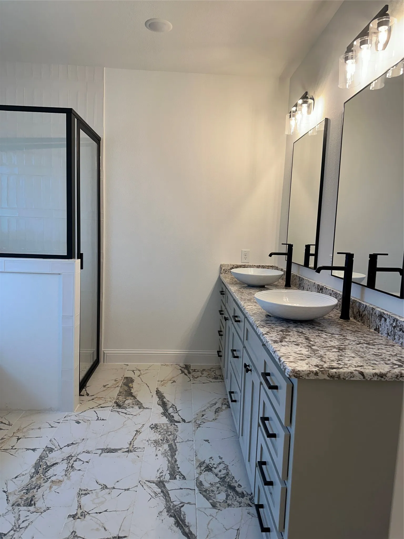 Double vanity with vessel sinks, matte black faucets and hardware, granite countertop, and marble-look tile flooring