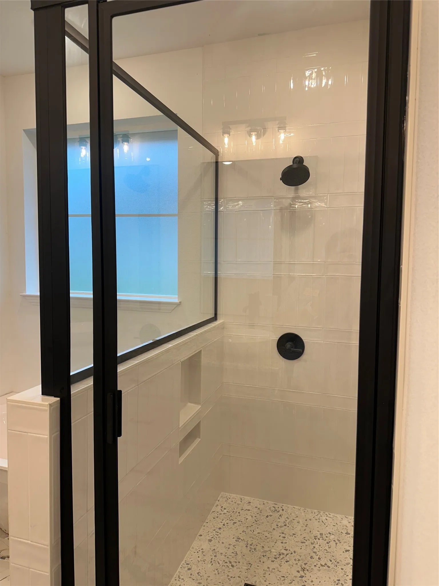 Modern shower enclosure with black-framed glass panels, contrasting white tile walls, a built-in shower niche, and a patterned shower floor