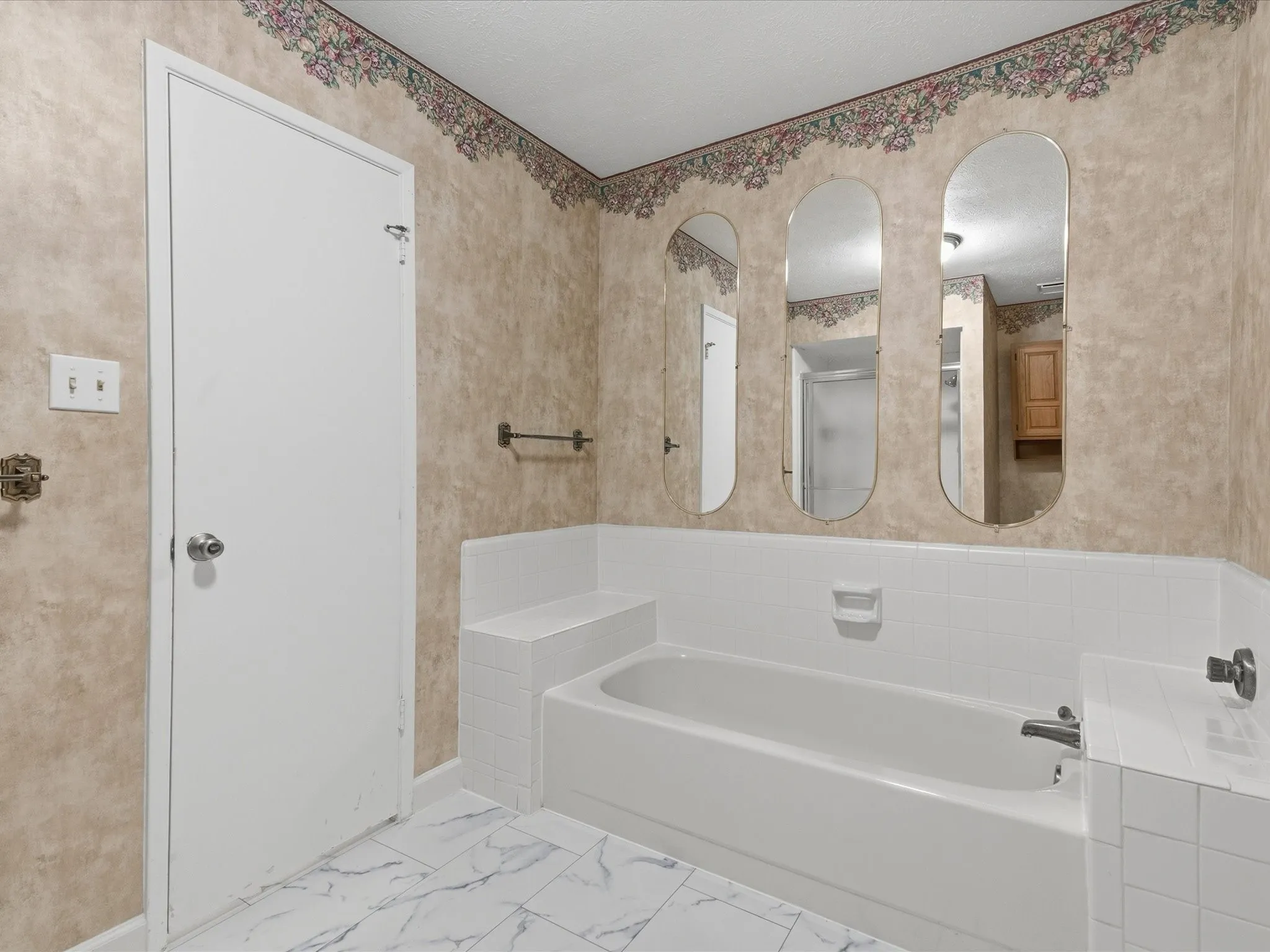 Bathtub with white tile surround, three wall-mounted arched mirrors, and white tile flooring