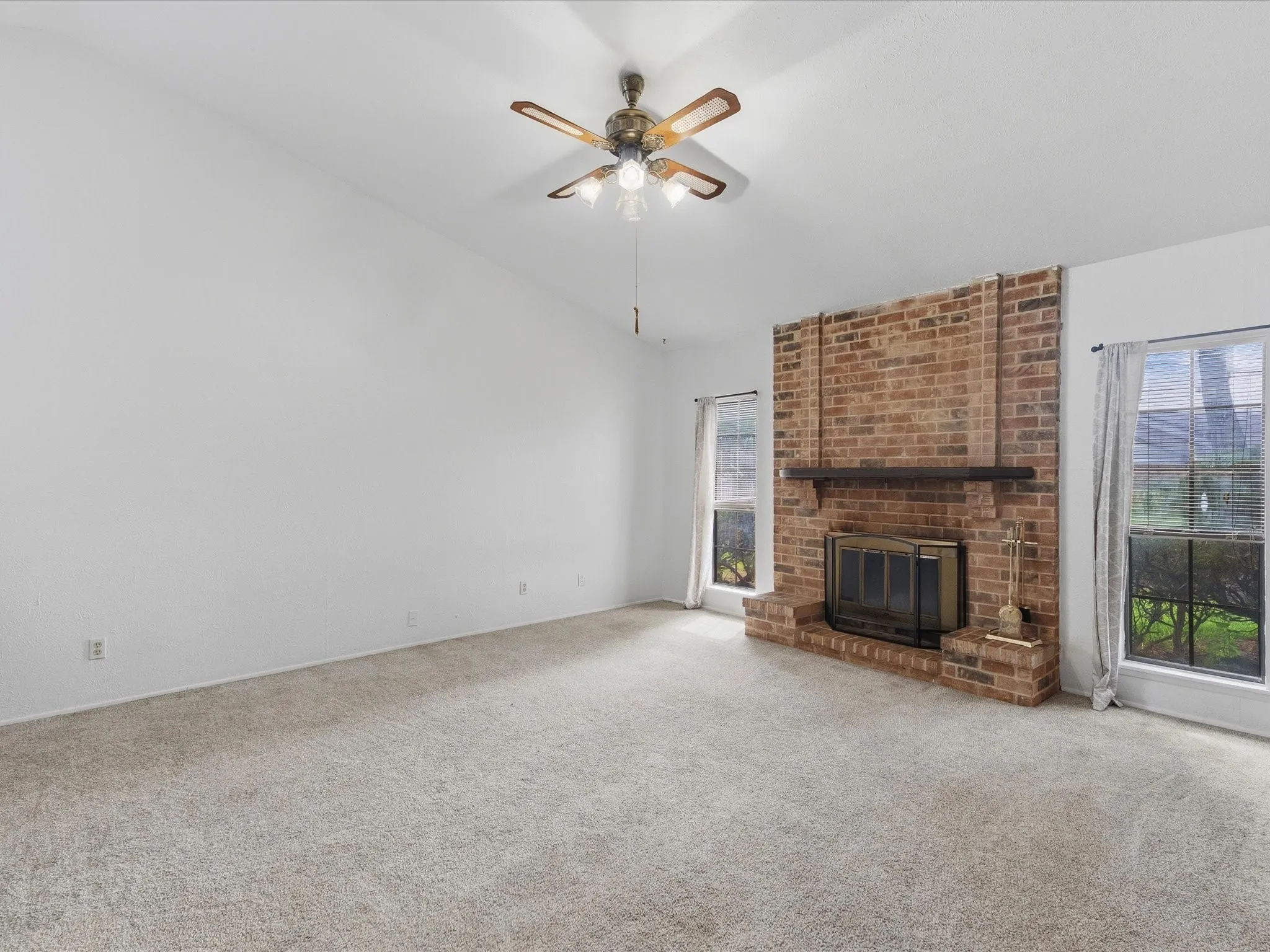 Vaulted ceilings with a ceiling fan, brick fireplace with a wood mantle, and multiple windows allowing natural illumination