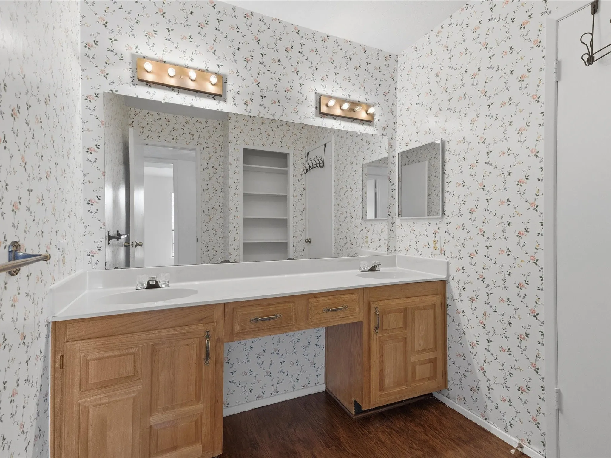 Dual sink vanity with wood-finish cabinetry, integrated countertop, and laminate flooring