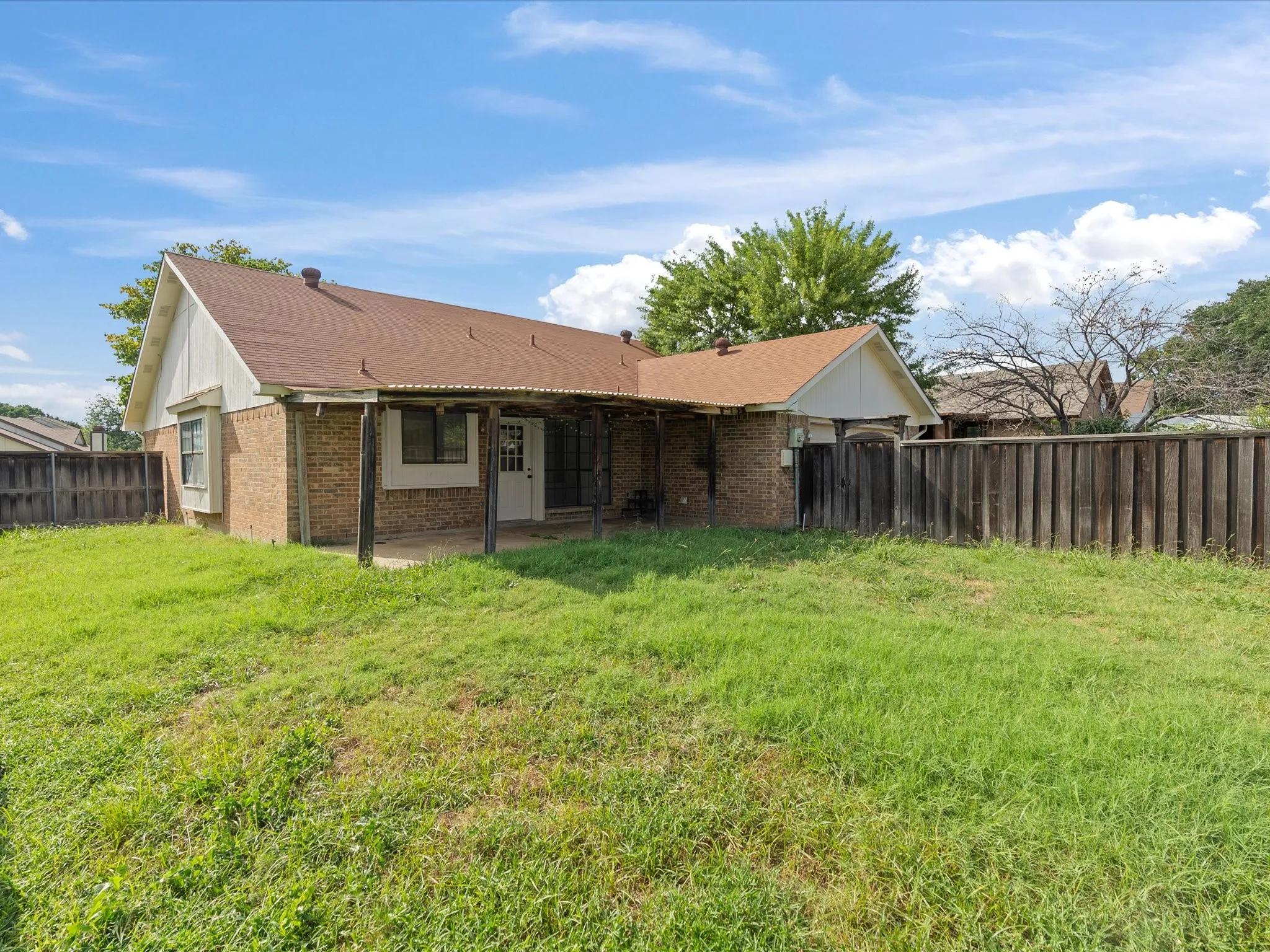 Brick exterior with a covered patio, wood fencing, and a grassy yard