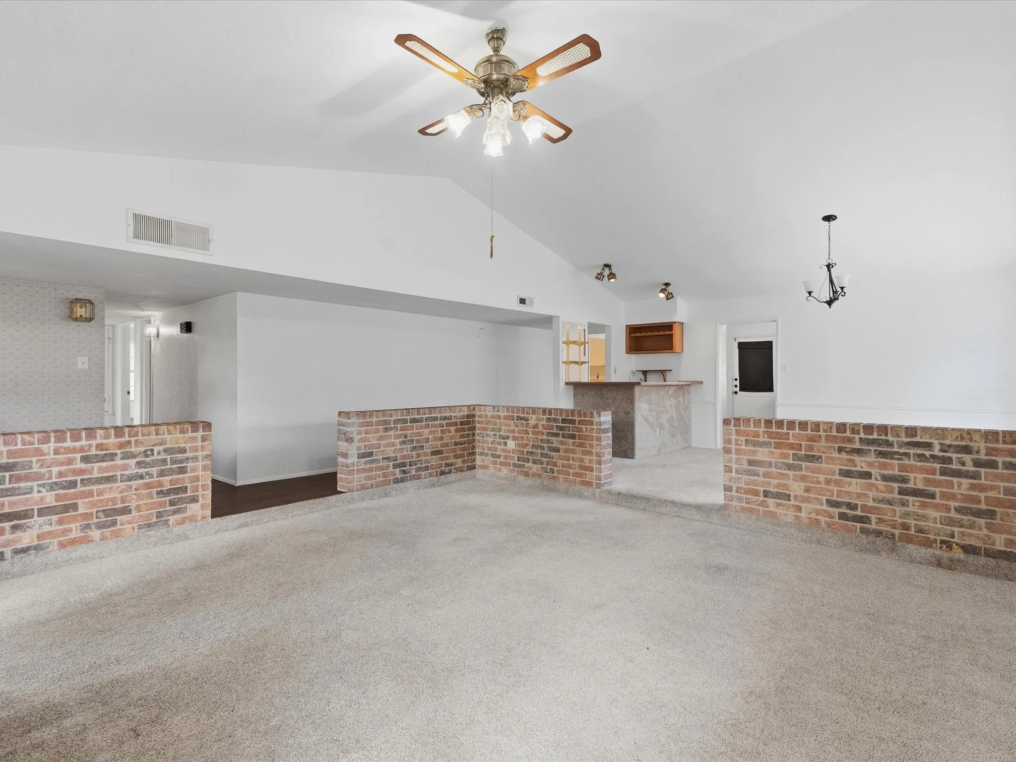 Vaulted ceilings, a built-in wet bar with wood cabinetry, and brick half-walls