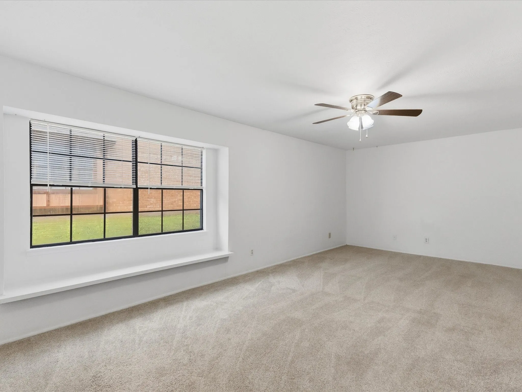 Expansive room featuring neutral-toned carpeting, a ceiling fan with light fixture, and a large window with horizontal blinds and a window ledge