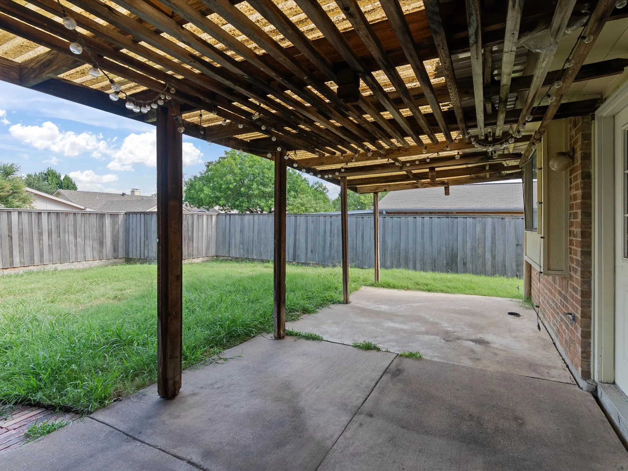 Covered concrete patio with wooden slat pergola and brick exterior