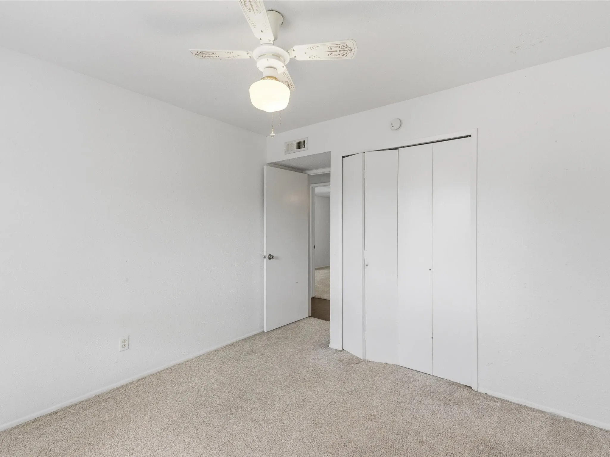 Plush neutral-toned carpeting, white walls, white bifold closet doors, and an overhead ceiling fan with lighting