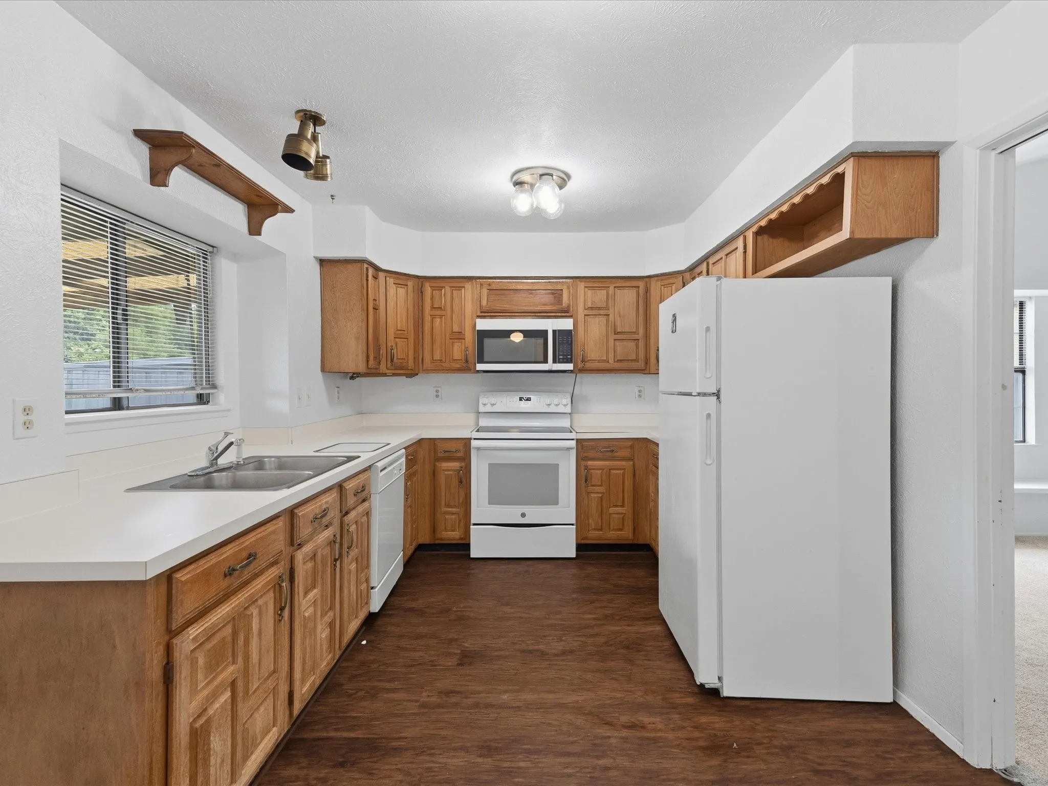 Kitchen featuring wood-finish cabinetry, white countertops, stainless steel sink, and white appliances