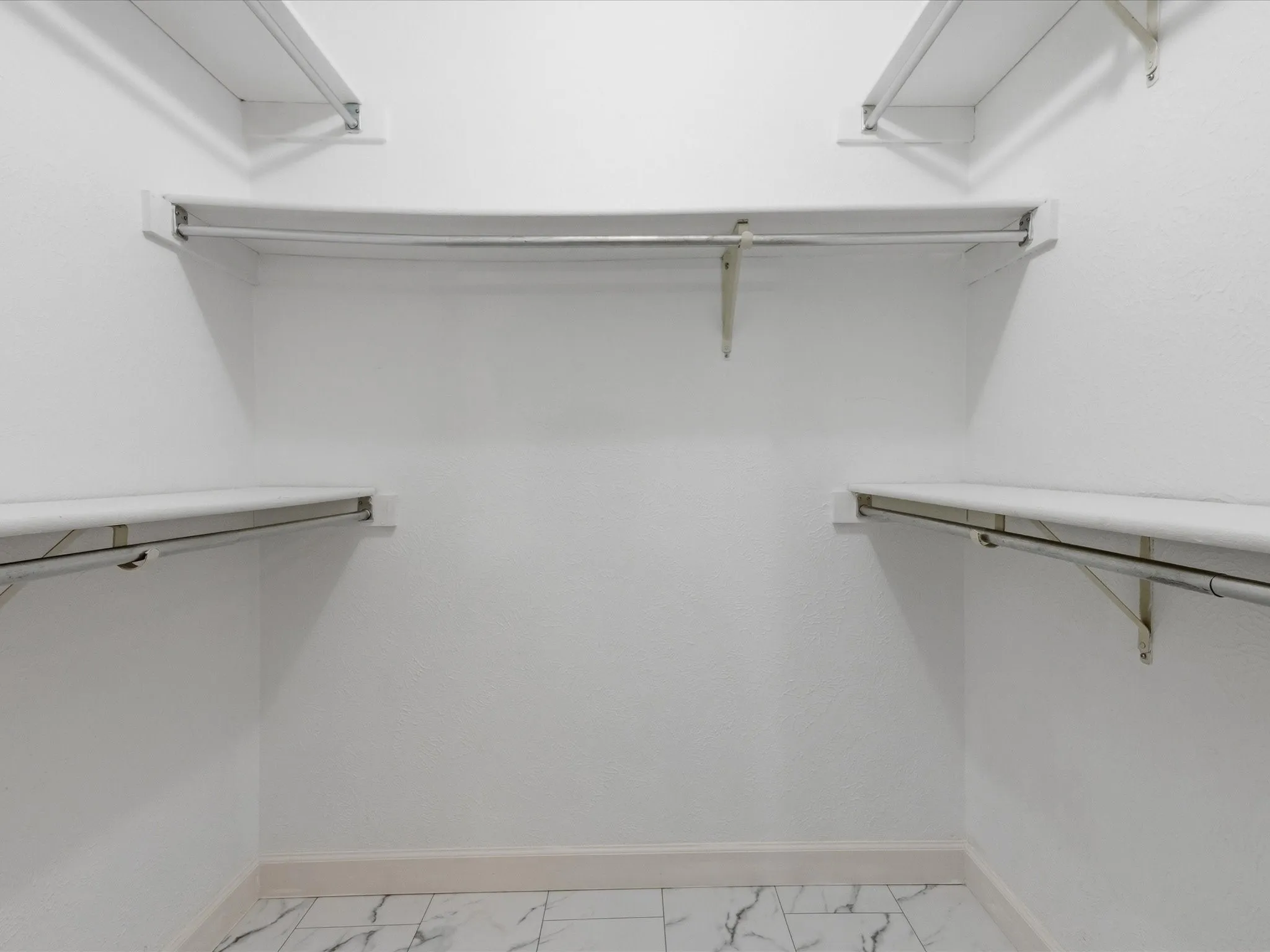 White shelving system with hanging rods, tile flooring, and white walls