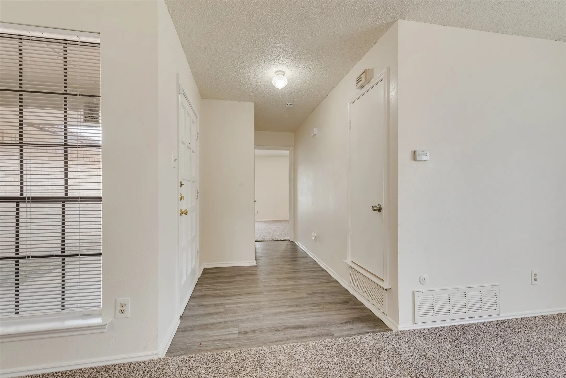 Entryway featuring wood-finish flooring, a white paneled door with brass hardware, and a window with horizontal blinds