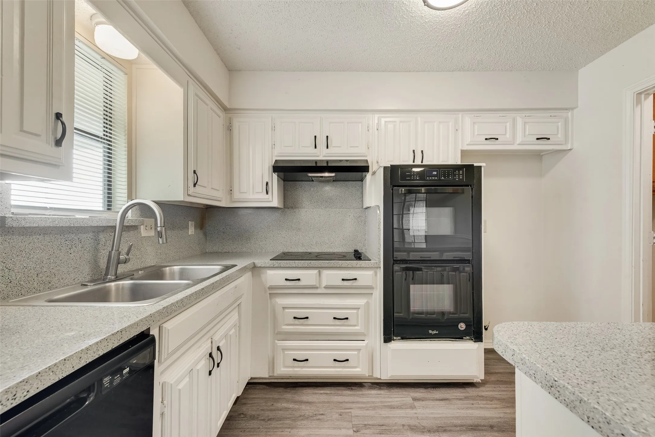 Kitchen featuring white cabinetry, light-toned countertops, a double basin sink, a built-in double oven, and wood-finish flooring