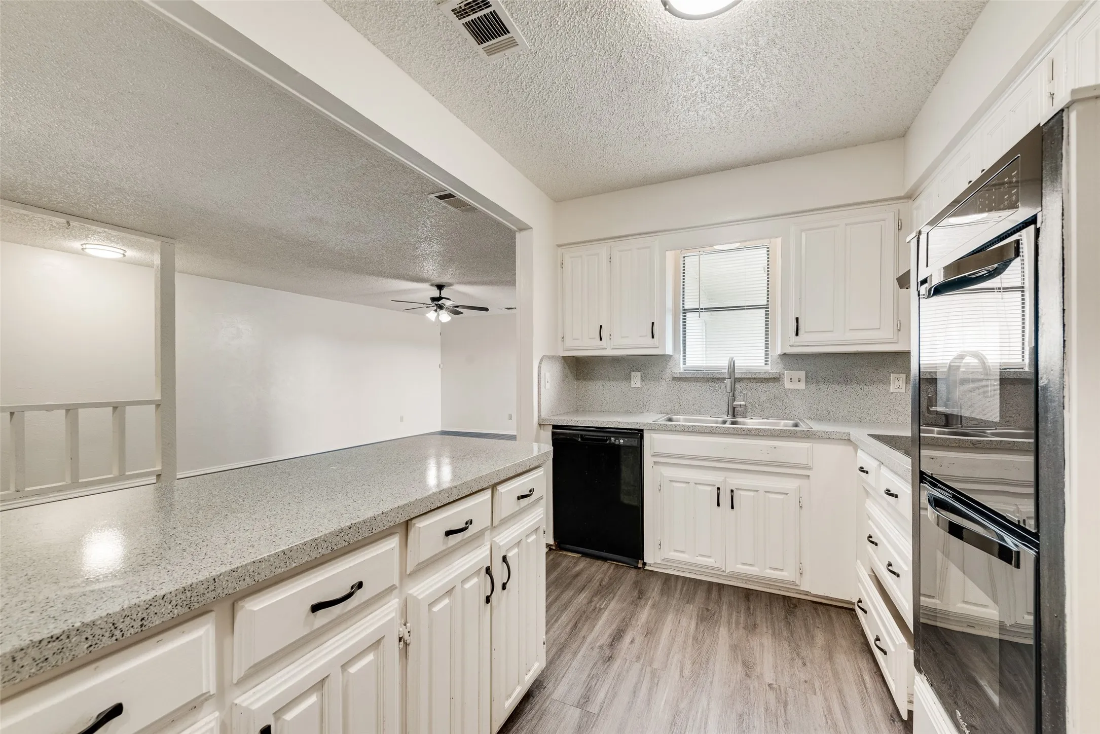 Kitchen featuring white cabinetry, gray speckled countertops, black appliances, and wood-finish flooring