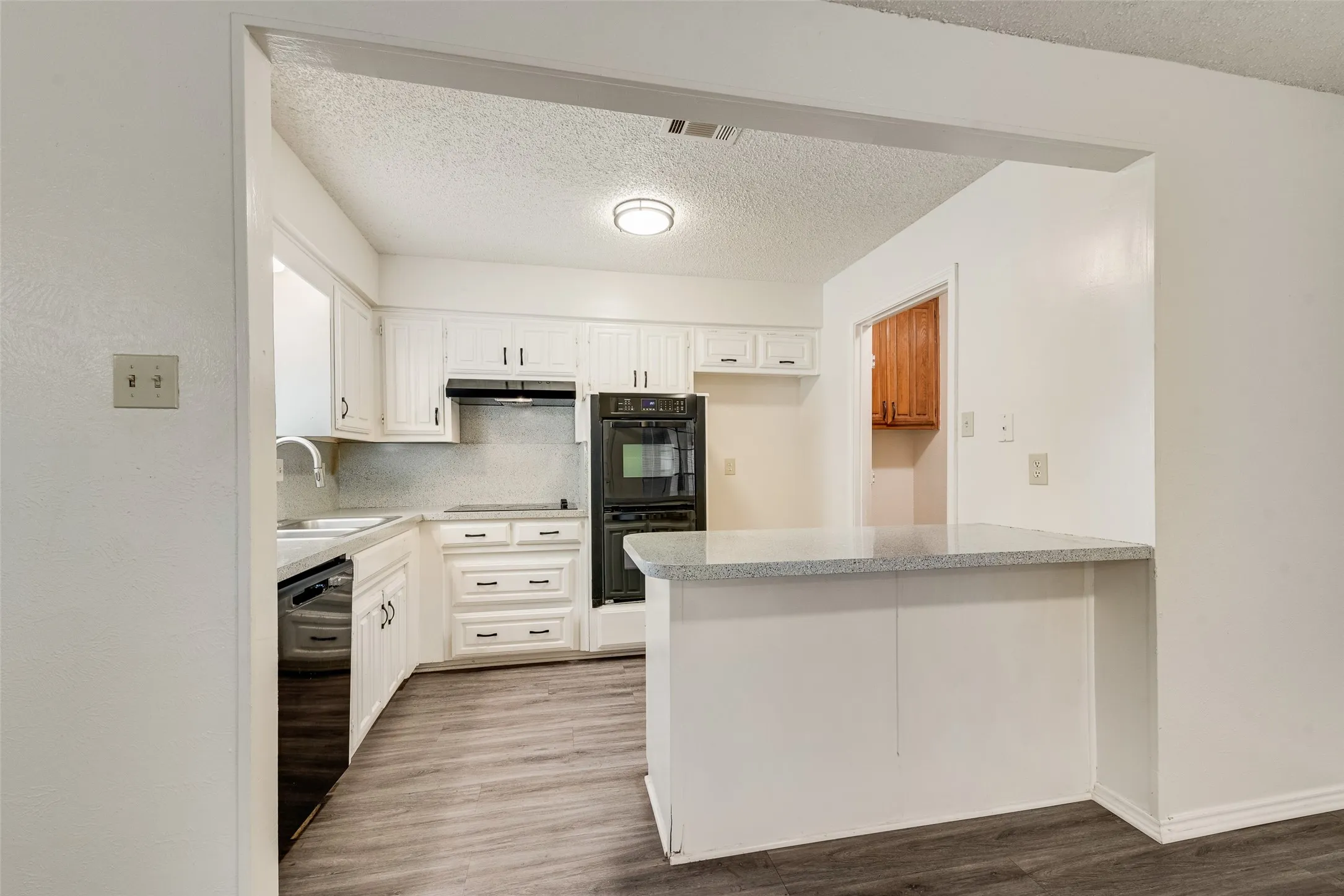 Kitchen featuring white cabinetry, stone-finish countertops, built-in double ovens, and wood-finish flooring