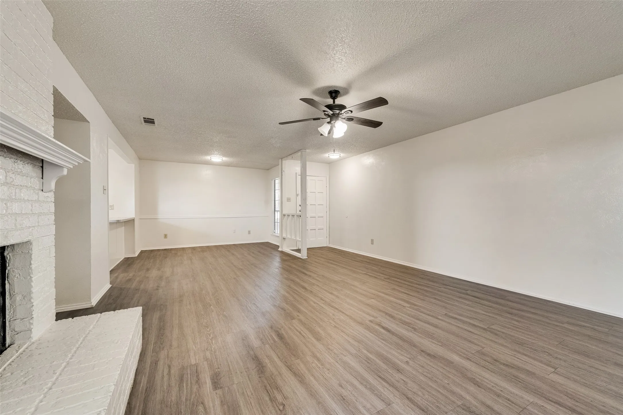 Expansive living space featuring wood-finish flooring, a painted brick fireplace, and a ceiling fan