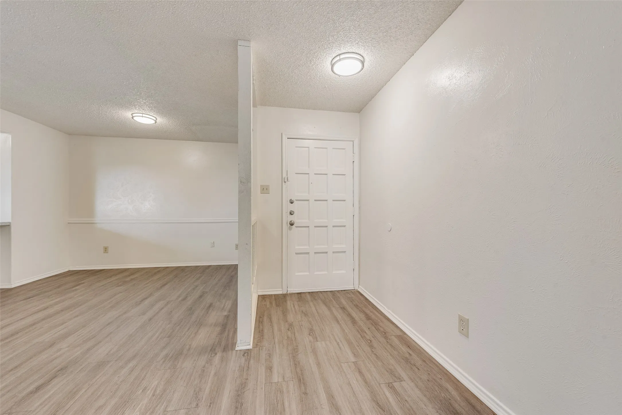 Wood-finish flooring throughout, white paneled entry door with multiple locks, and a half wall partition
