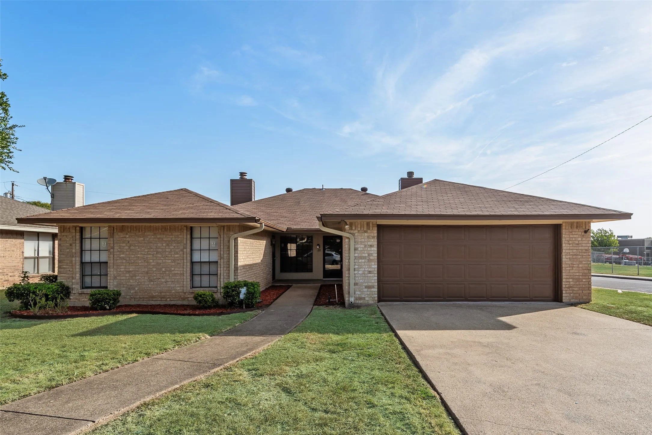 Brick exterior, brown asphalt shingle roof, attached two-car garage, concrete driveway, and a concrete pathway to the entrance
