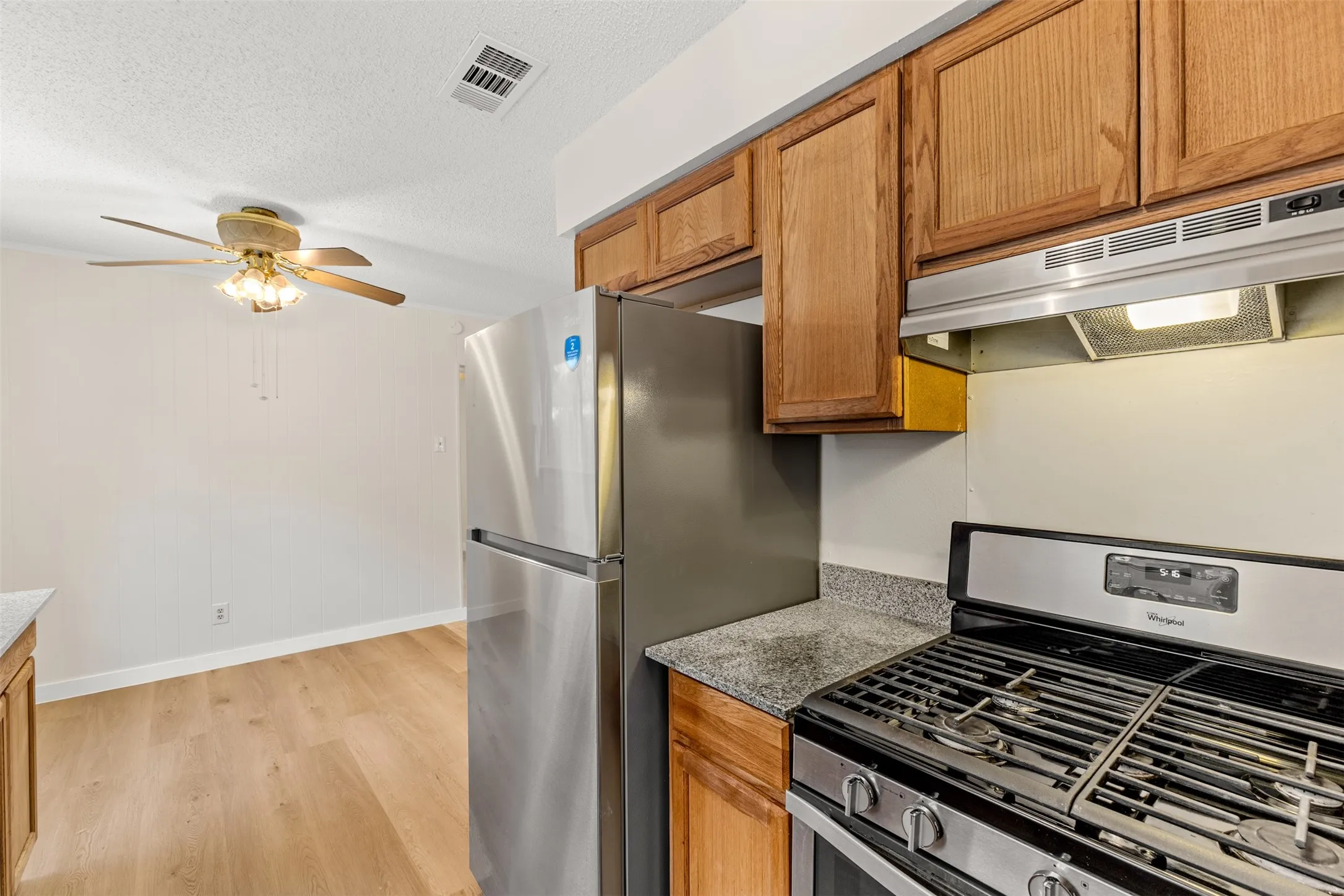 Dining area attached to kitchen, Stainless steel gas range, overhead exhaust hood, wood cabinetry, stone-finish countertops, and wood-finish flooring