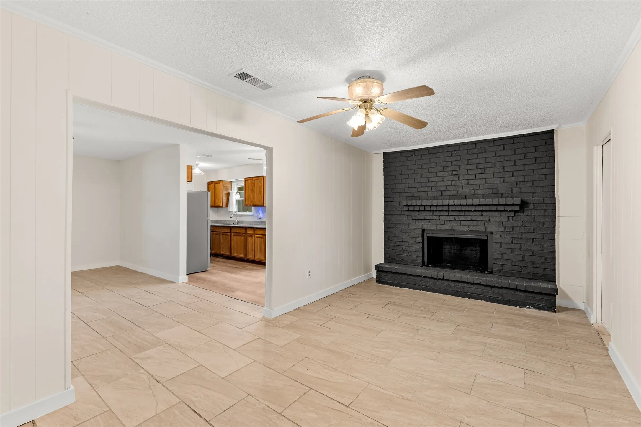 Spacious room featuring tile flooring, a black brick fireplace, and a ceiling fan