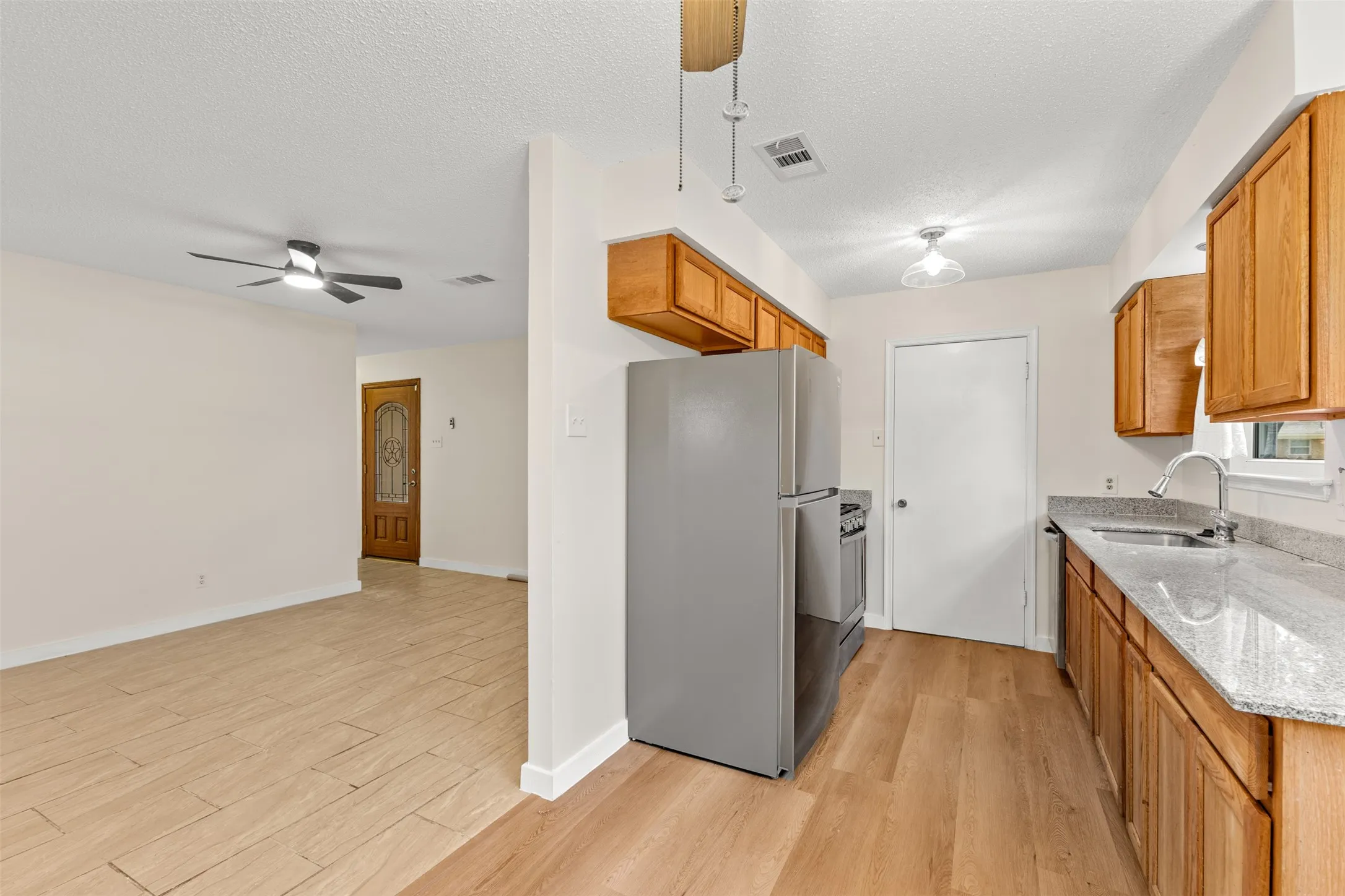 Kitchen featuring wood-finish flooring, wood cabinetry, stone countertops, and a stainless steel sink