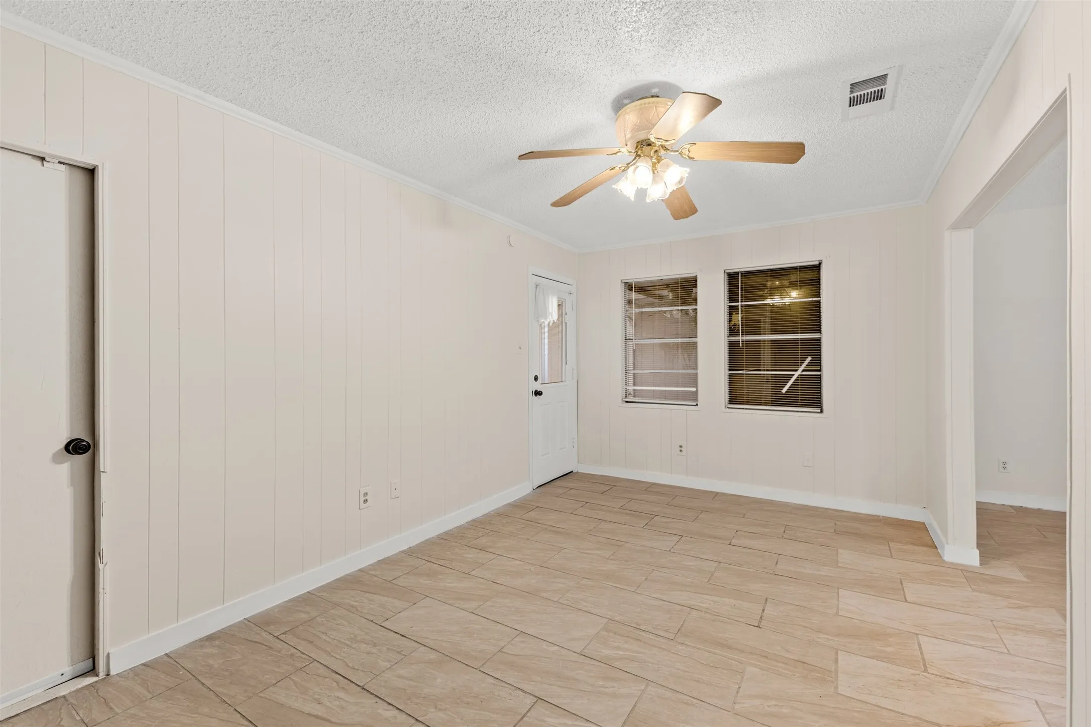 Tile flooring, vertical paneling, two windows, ceiling fan, and recessed doorway
