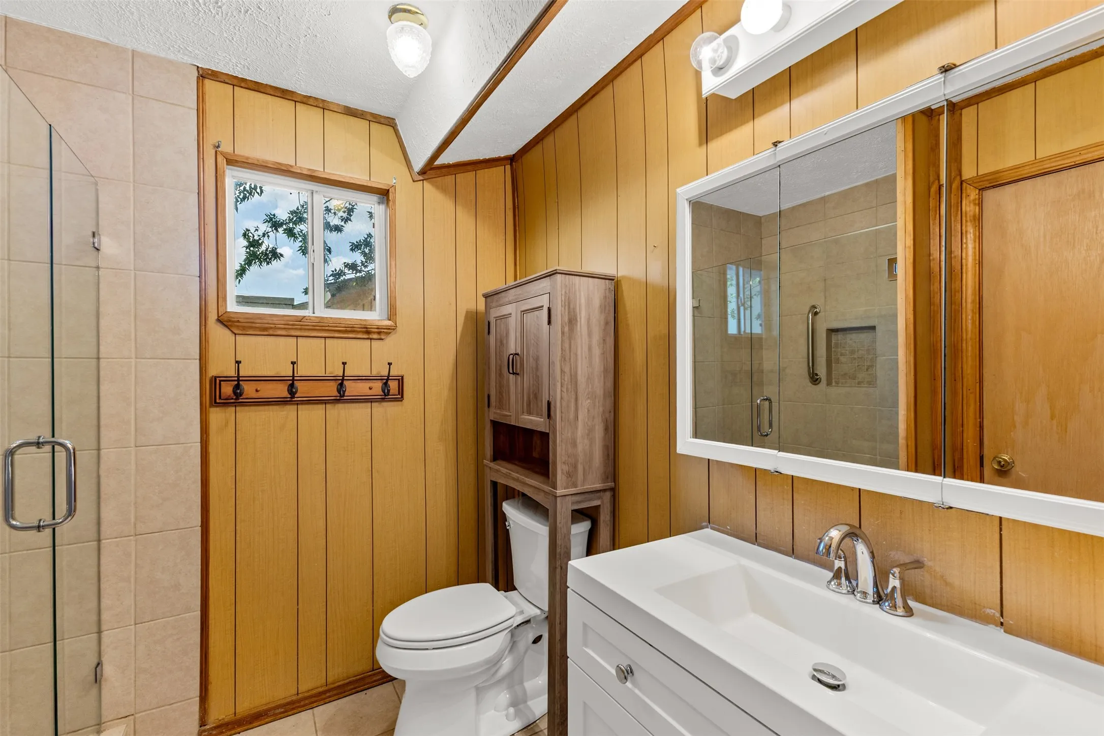 Glass-enclosed shower with tile surround, white vanity with integrated sink, chrome-finish faucet, and wood-paneled walls