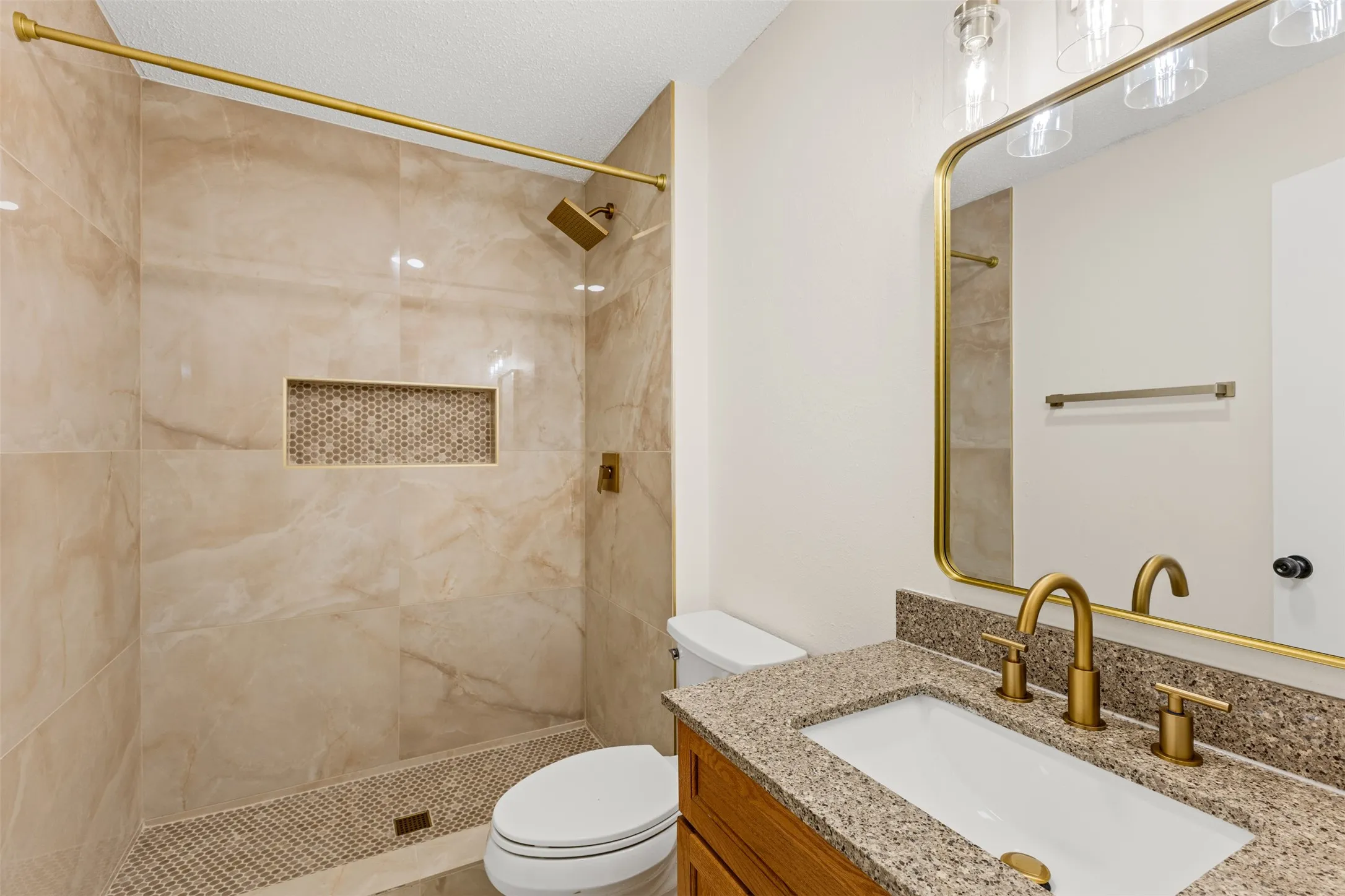 Walk-in shower with large format tile, mosaic-tiled niche, and gold-finish fixtures
