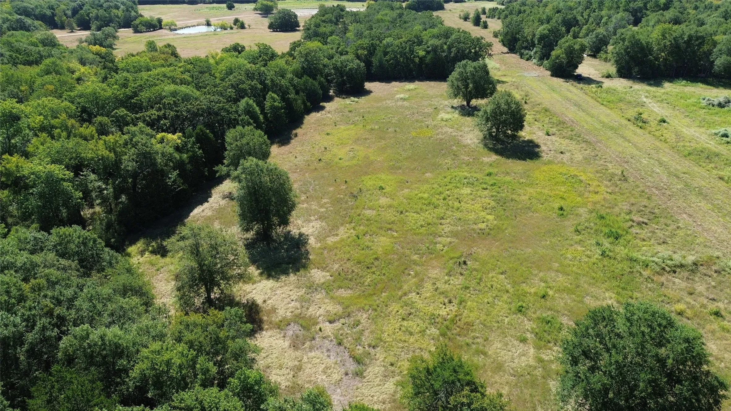 Expansive land parcel featuring open fields, mature trees, dense wooded areas, and a visible pond