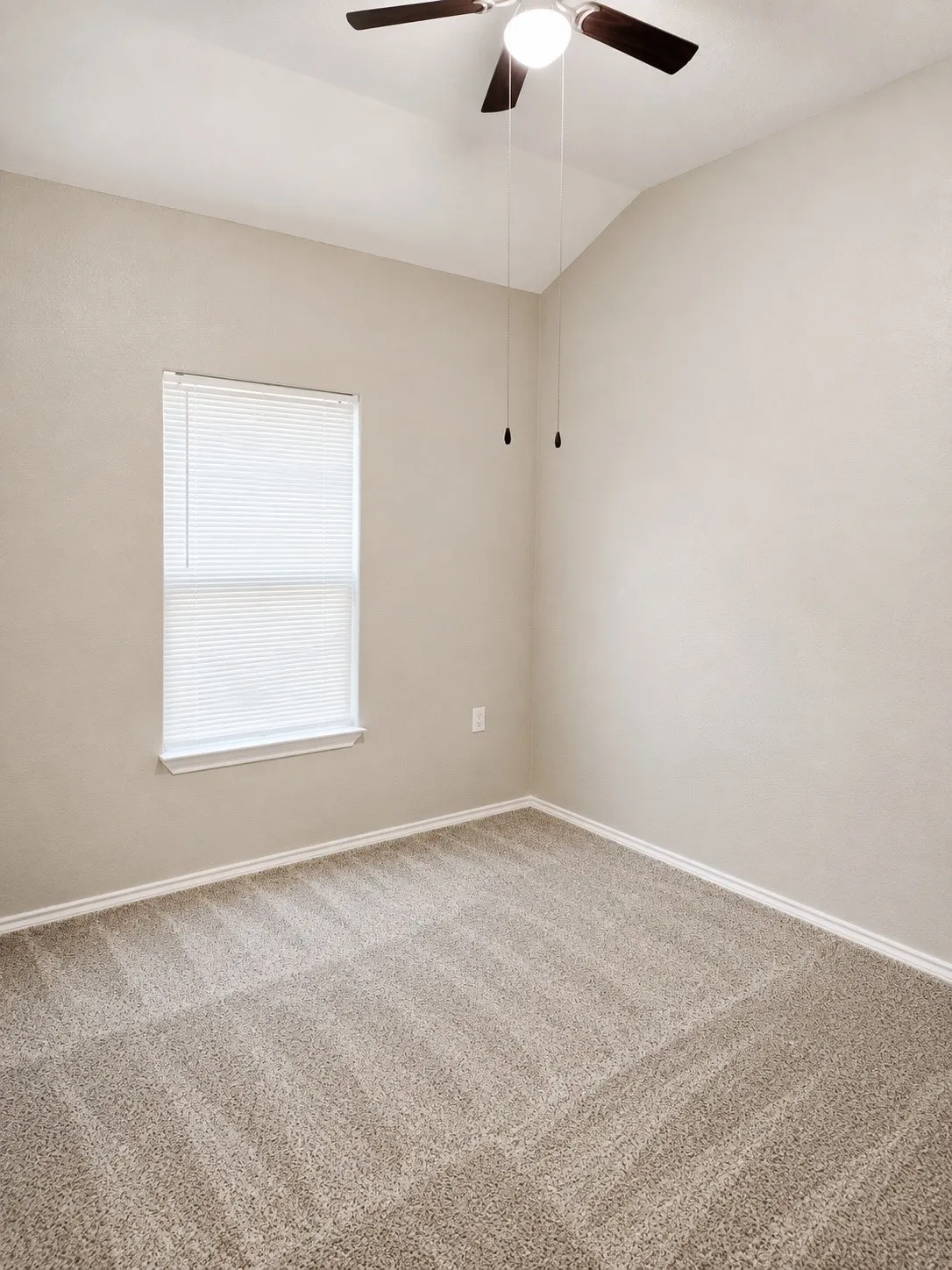 Vaulted ceiling featuring a ceiling fan with integrated lighting, neutral wall paint, window with blinds, and carpeting
