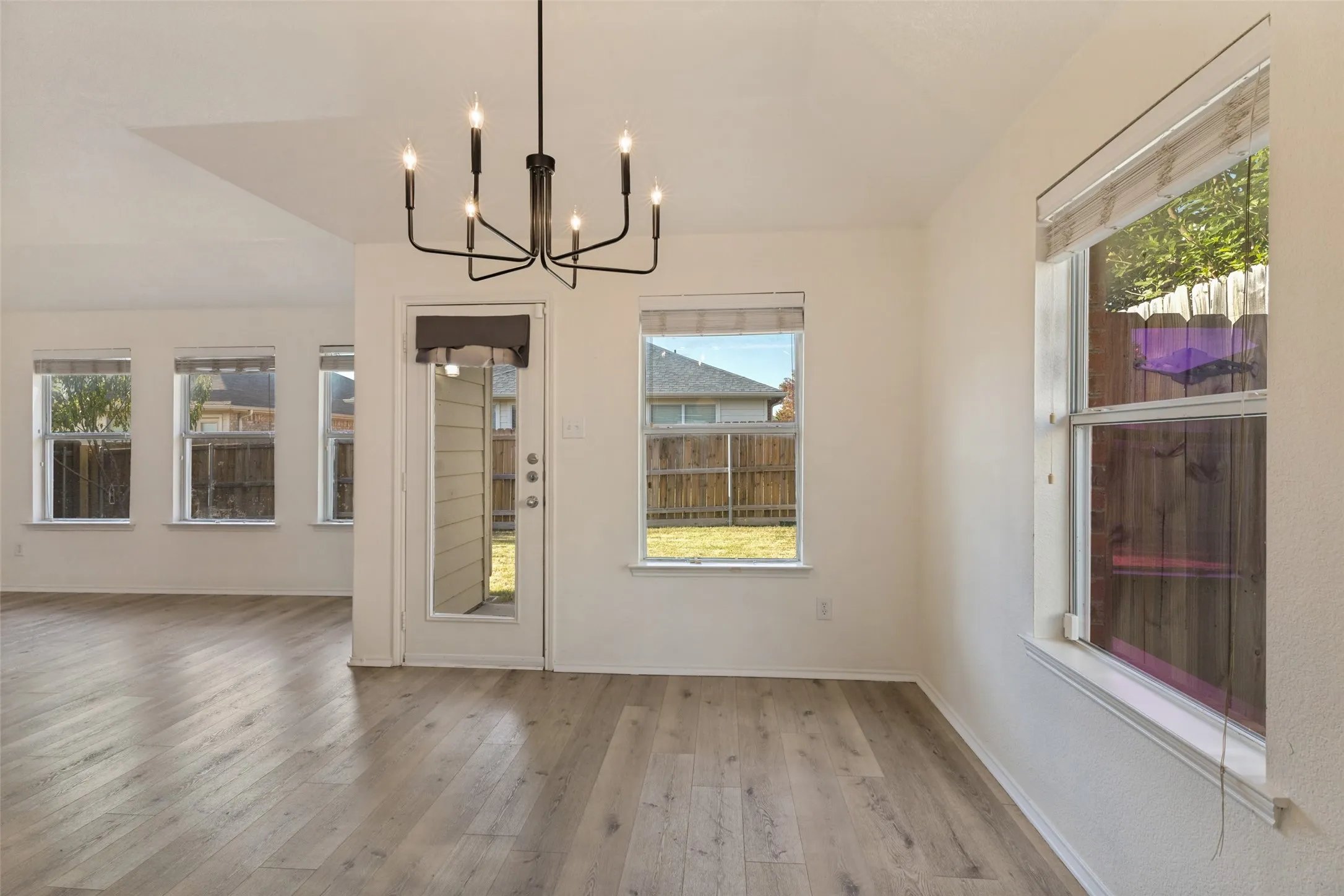 Open-concept living area featuring wood-finish flooring, multiple windows, a rear exterior door, and a modern chandelier