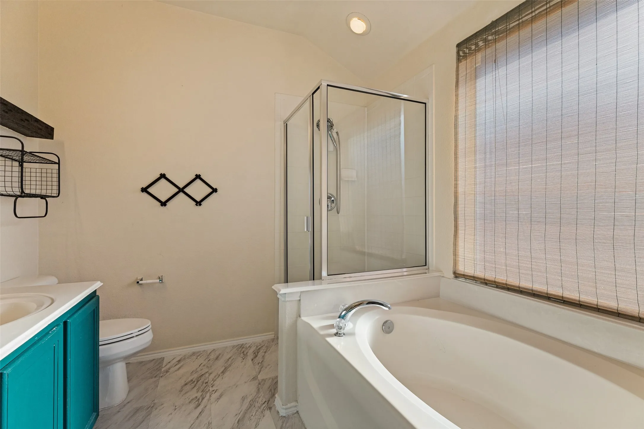 Spacious bathroom featuring a built-in tub, separate glass-enclosed shower, single vanity with a teal cabinet, and wood-finish flooring
