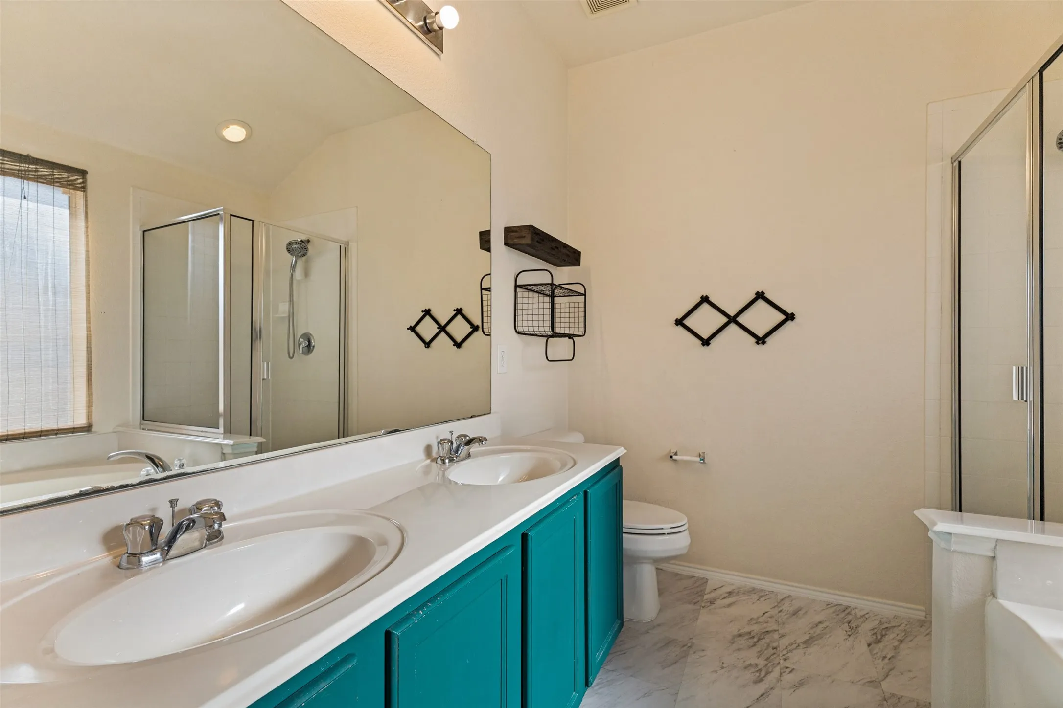 Dual undermount sinks, spacious vanity with teal cabinetry, large mirror, glass-enclosed shower, and a separate bathtub