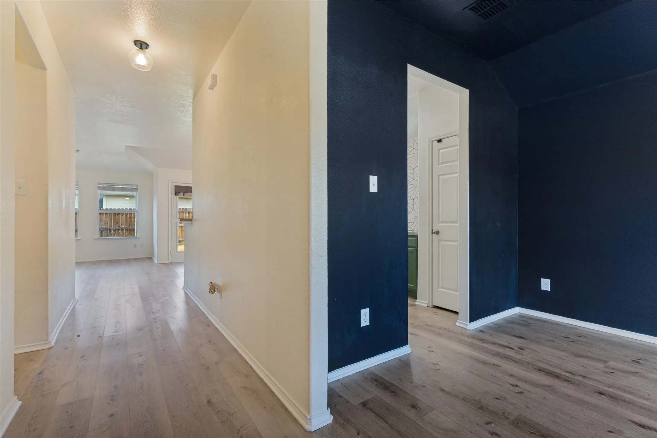 Wood-finish flooring throughout, light-colored walls in the main hallway, and a room with dark blue walls