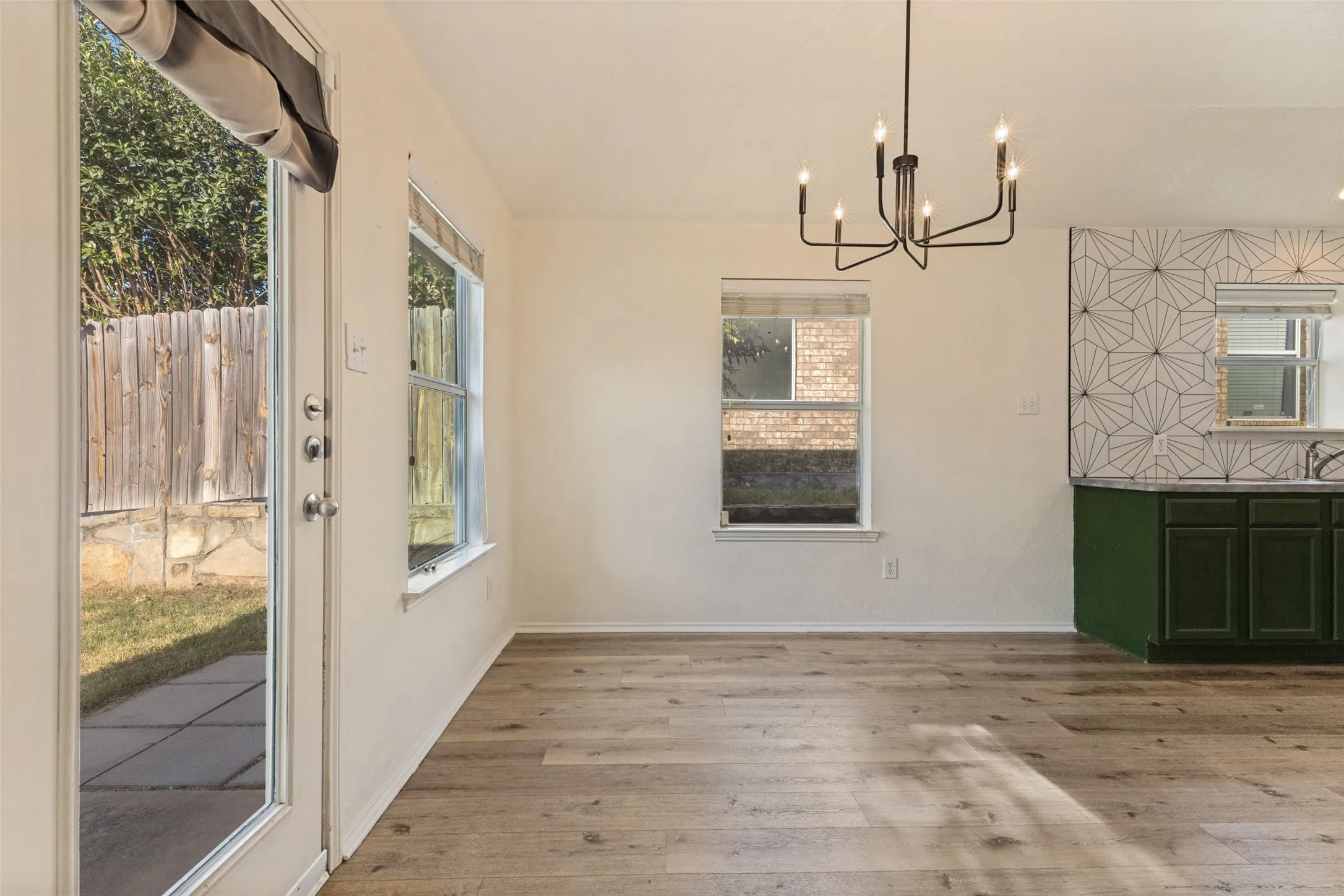 Wood-finish flooring, contemporary black chandelier, geometric tile backsplash, dark green cabinetry, and glass-paneled rear door