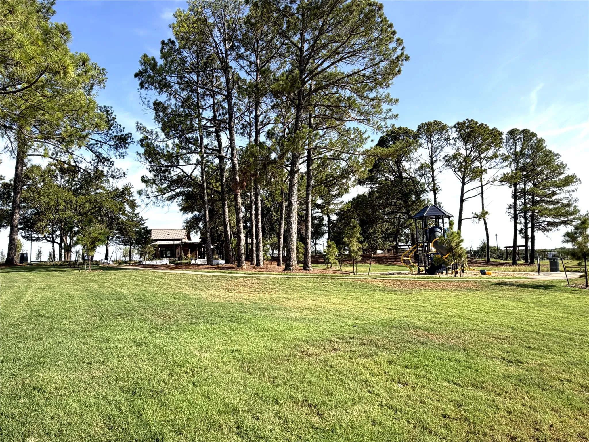Community Expansive green space featuring a natural tree line, playground structure, and a building with a covered patio