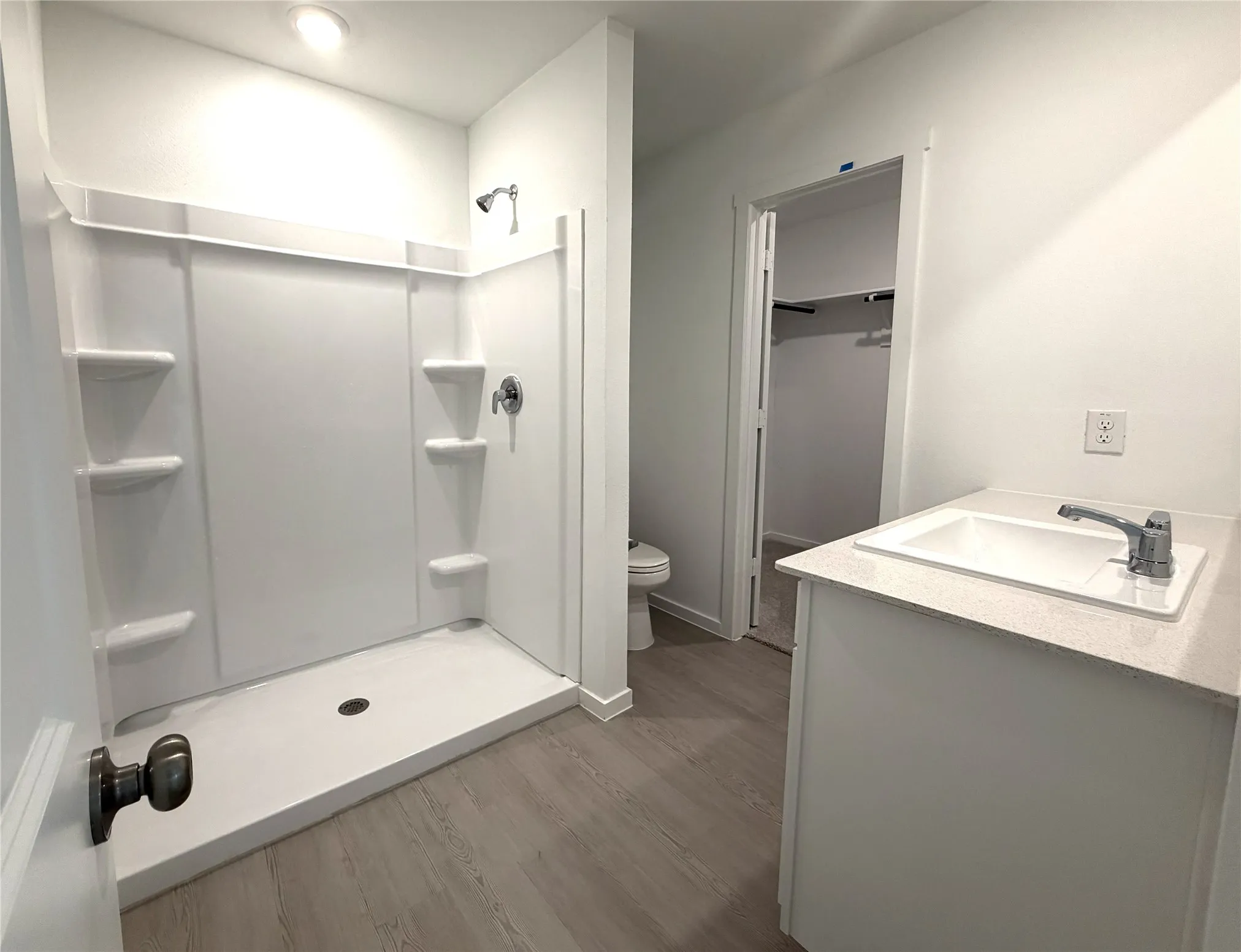 Bathroom with a walk-in shower featuring built-in shelving, a vanity with an integrated sink and countertop, wood-finish flooring, and a recessed ceiling light
