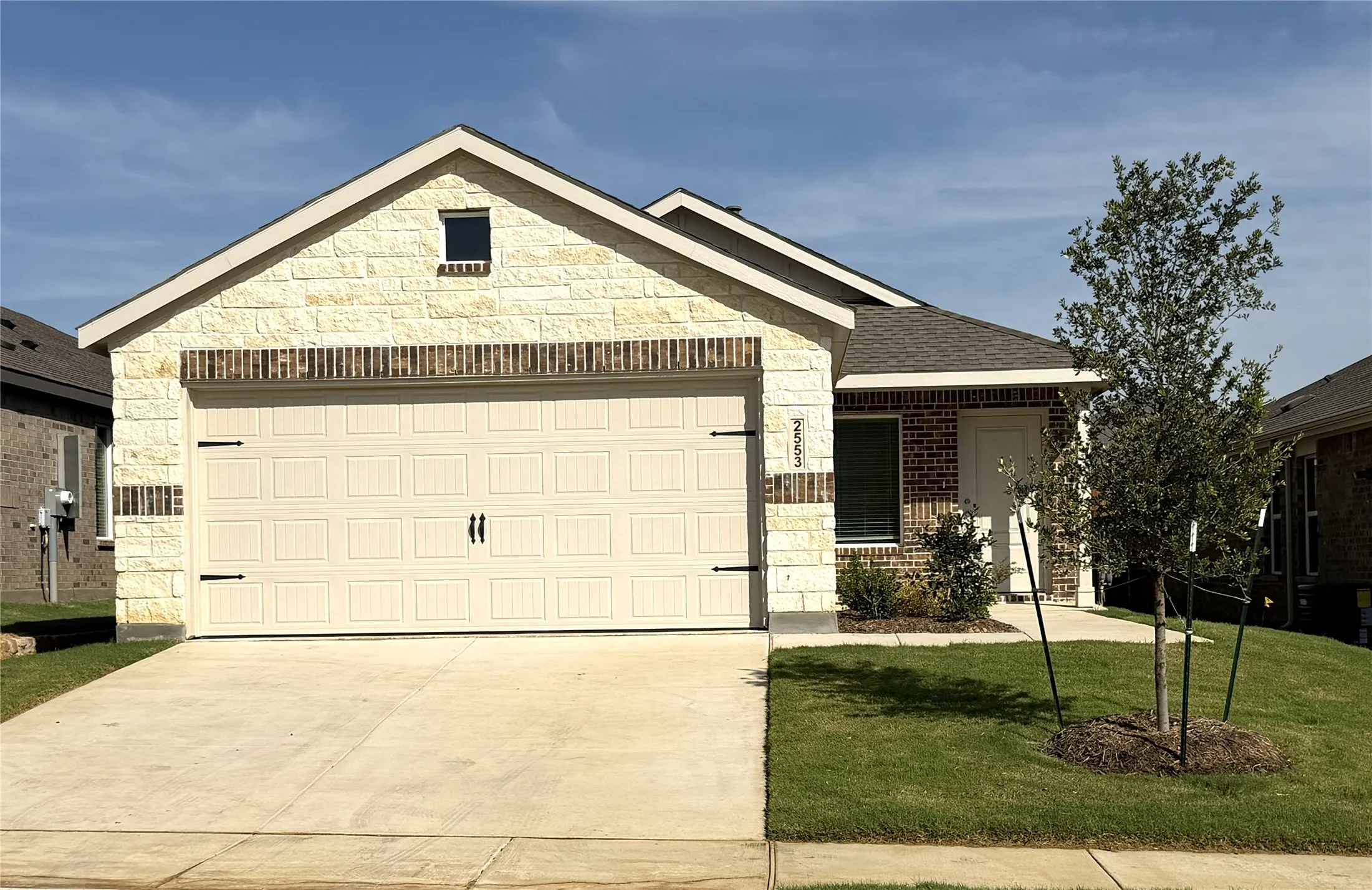 Exterior featuring a combination of light-colored stone and brick veneer, an attached garage with decorative hardware, a concrete driveway, and a well-maintained lawn
