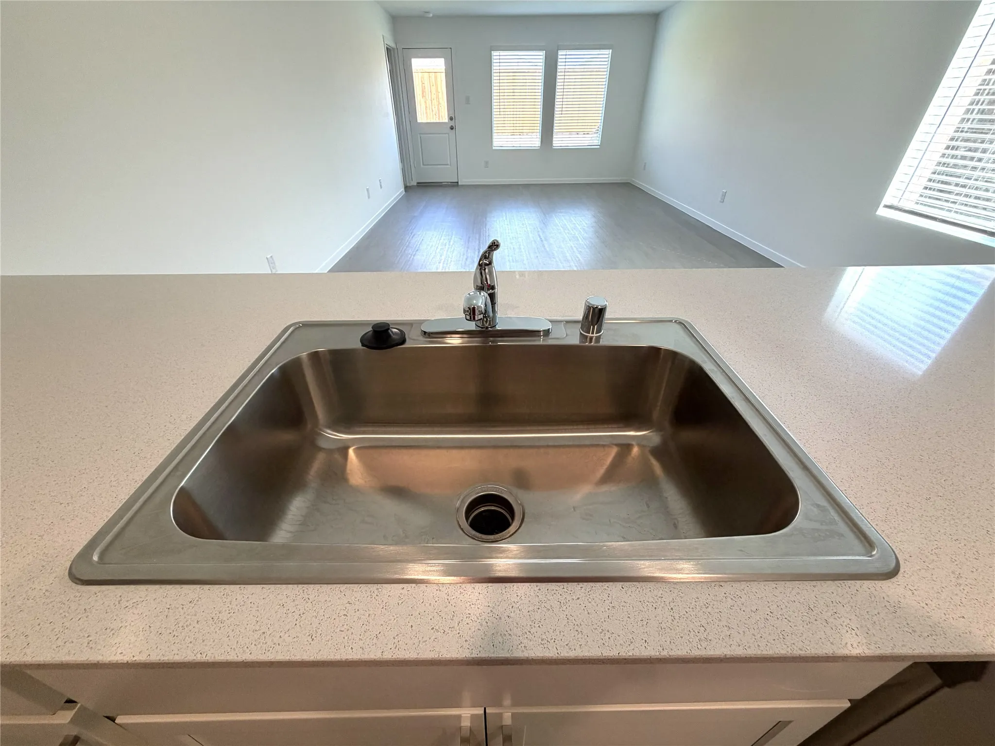 Stainless steel sink with a single-handle faucet, light-toned countertop, and white cabinetry