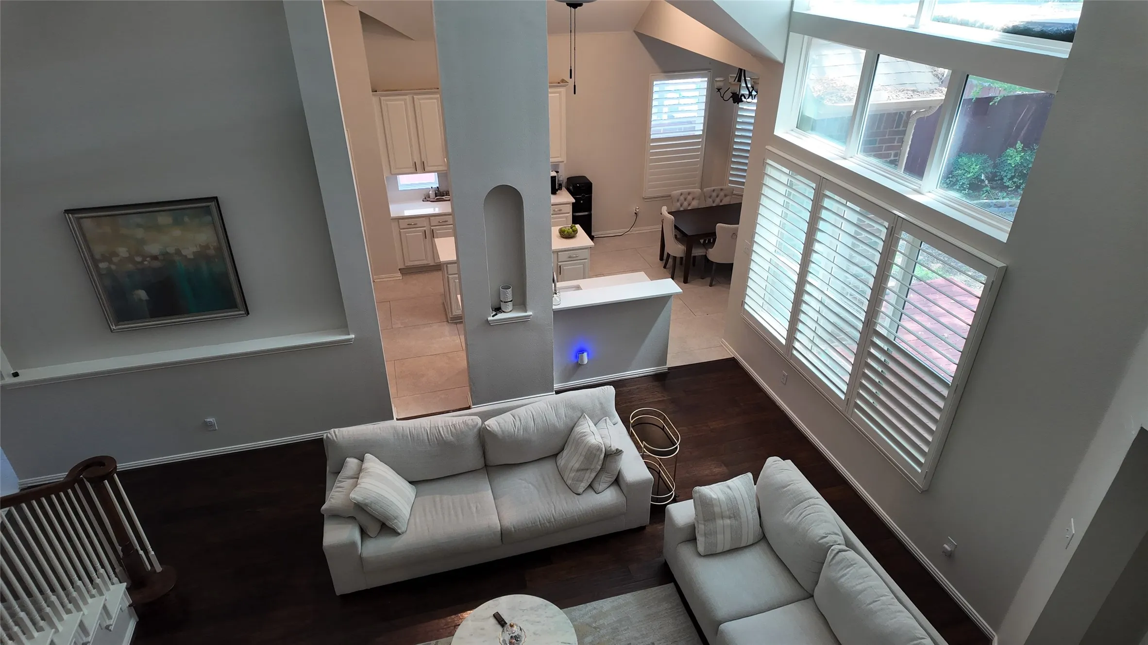 Vaulted ceilings with clerestory windows, dark wood-finish flooring, white plantation shutters, and a partial view of a kitchen with light cabinetry