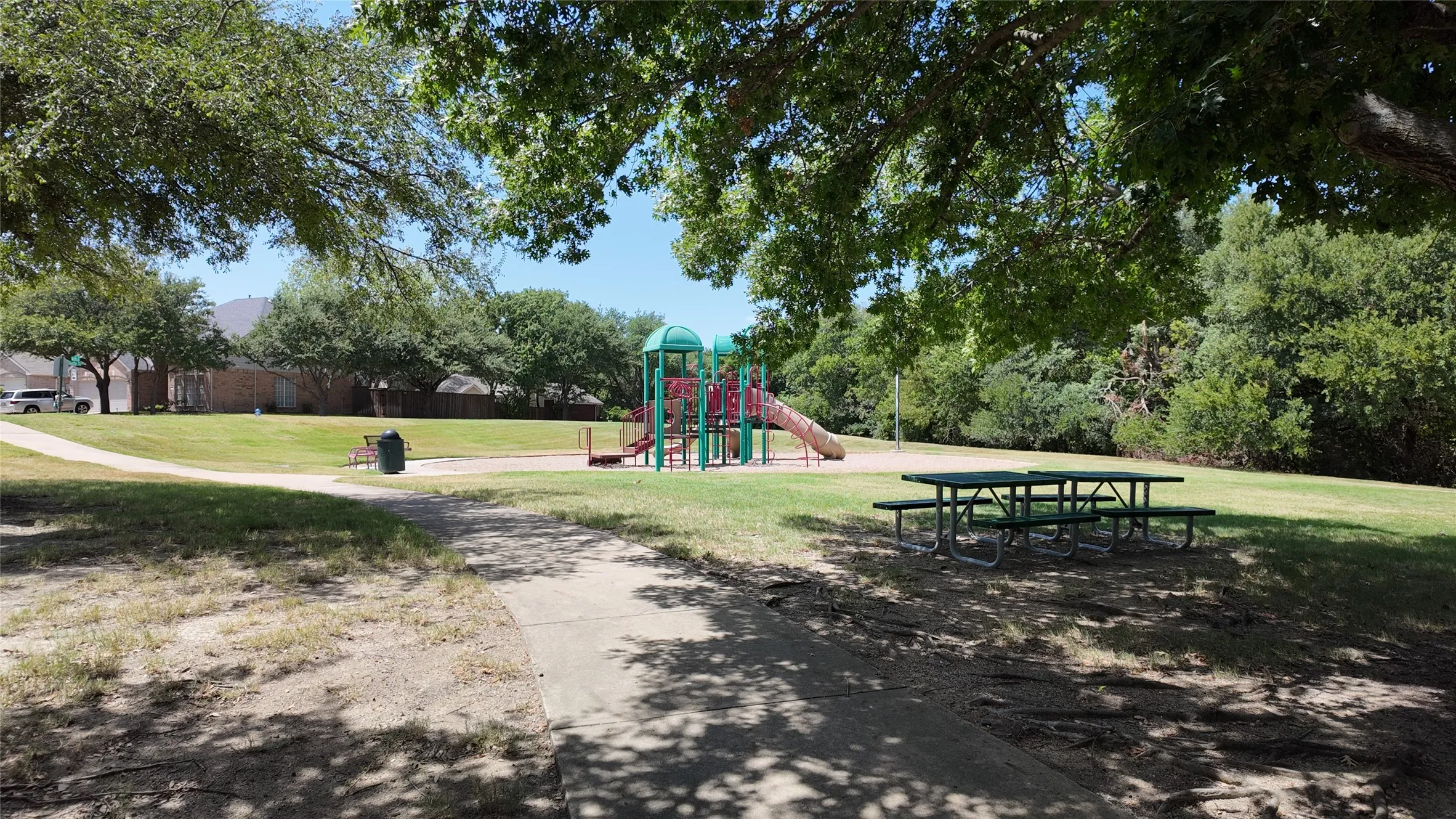 Community green space featuring mature trees, a playground structure, and picnic tables