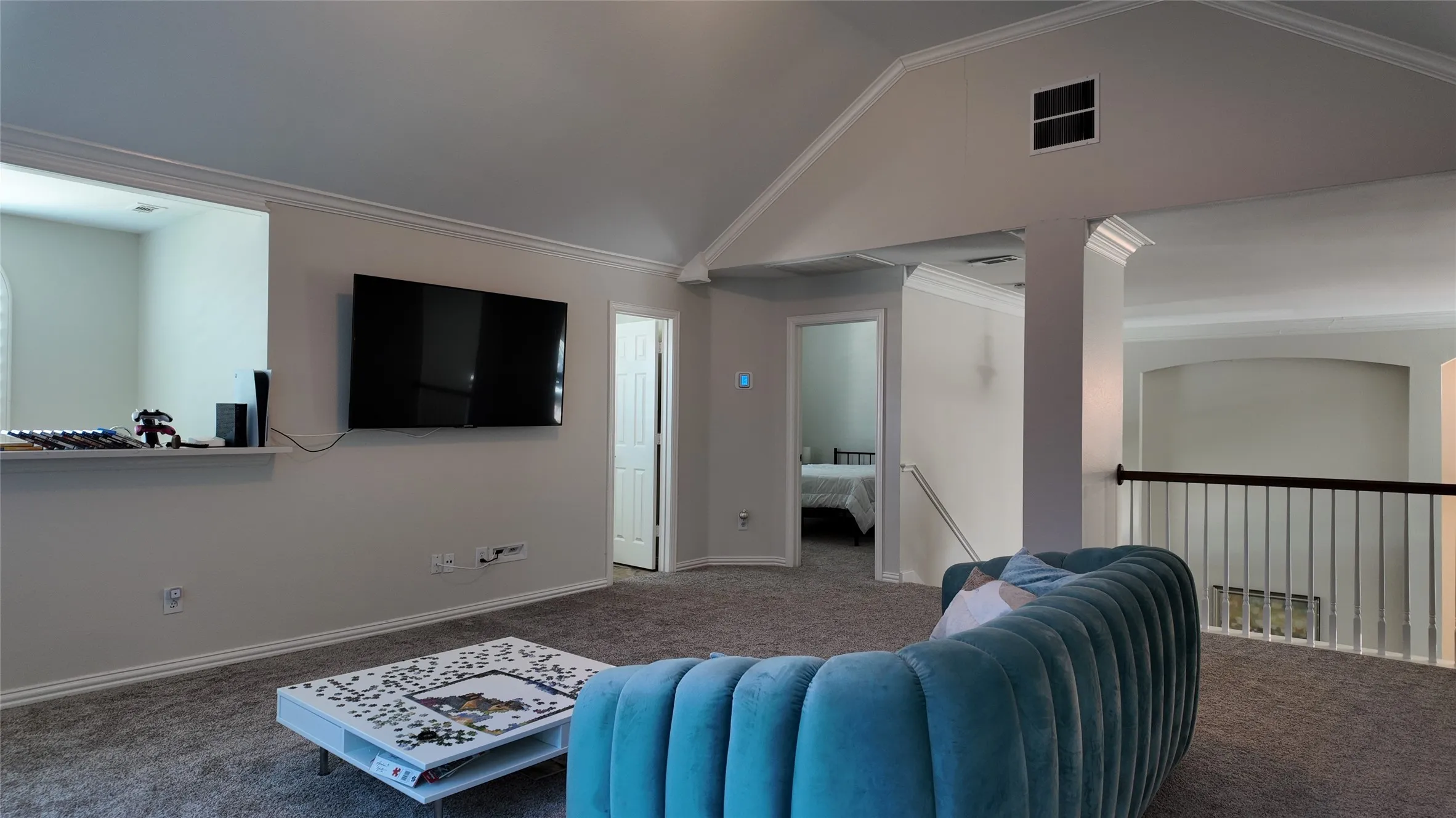 Vaulted ceiling, crown molding, wall-mounted television, interior balcony with metal spindles, and carpeted flooring