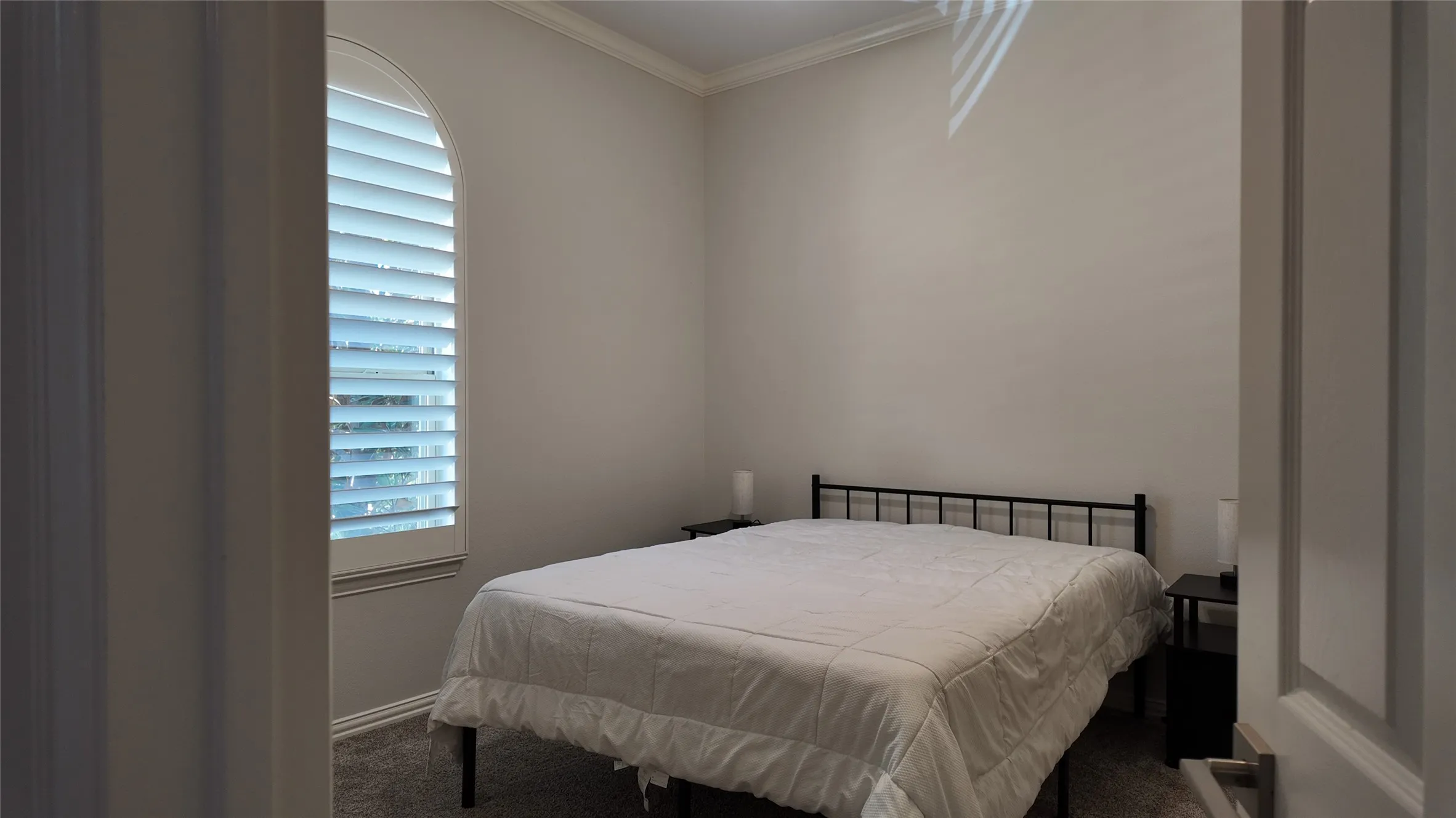 Arched window with plantation shutters, crown molding, and neutral wall tones