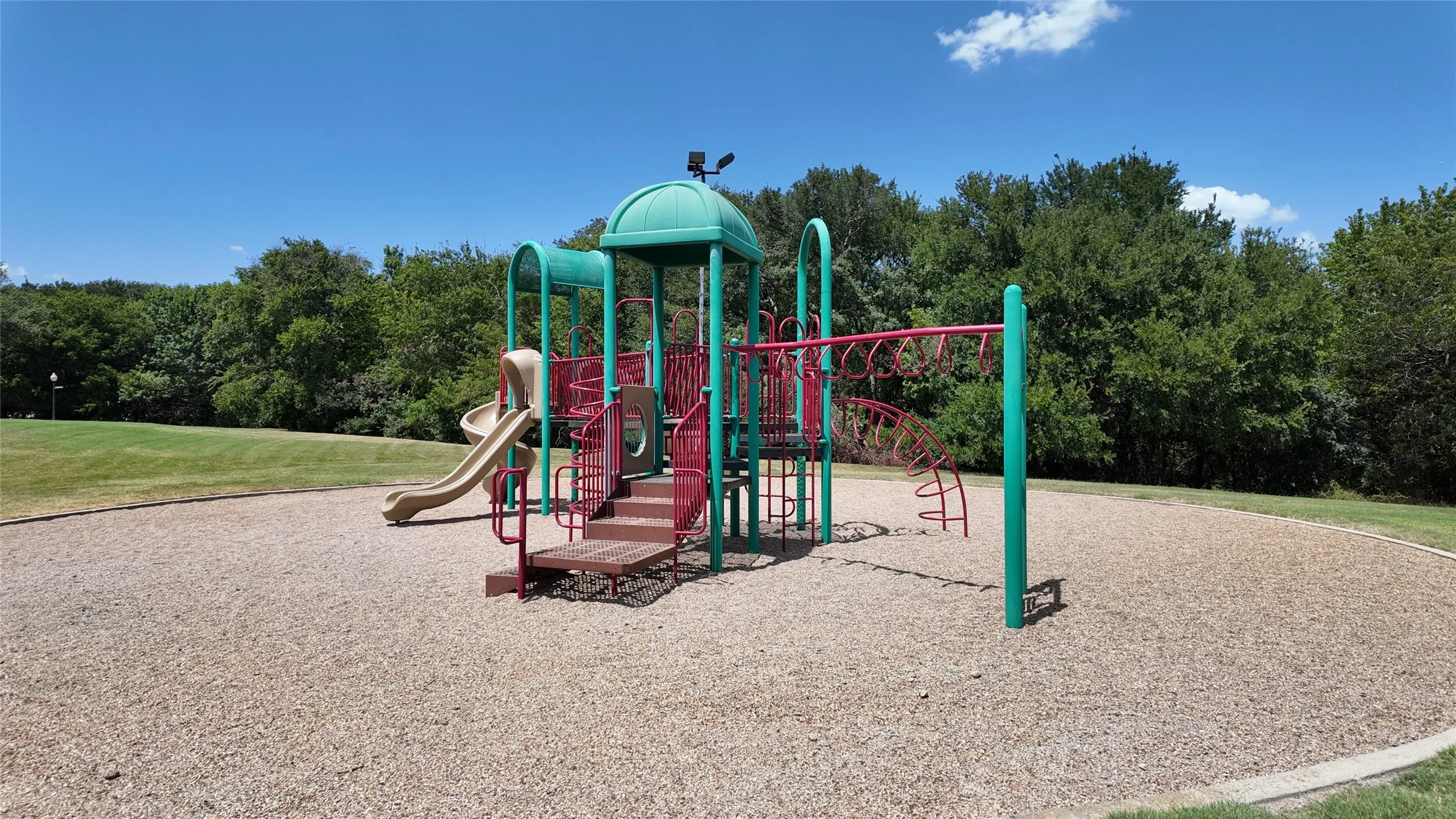Recreational playground featuring a slide, climbing structures, and monkey bars, set on a wood chip surface