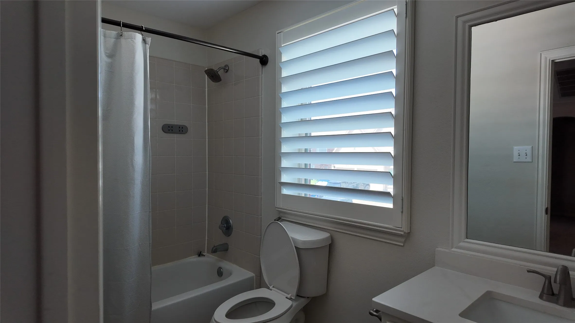 Bathtub with white subway tile surround, white window shutters, and a vanity with a white countertop
