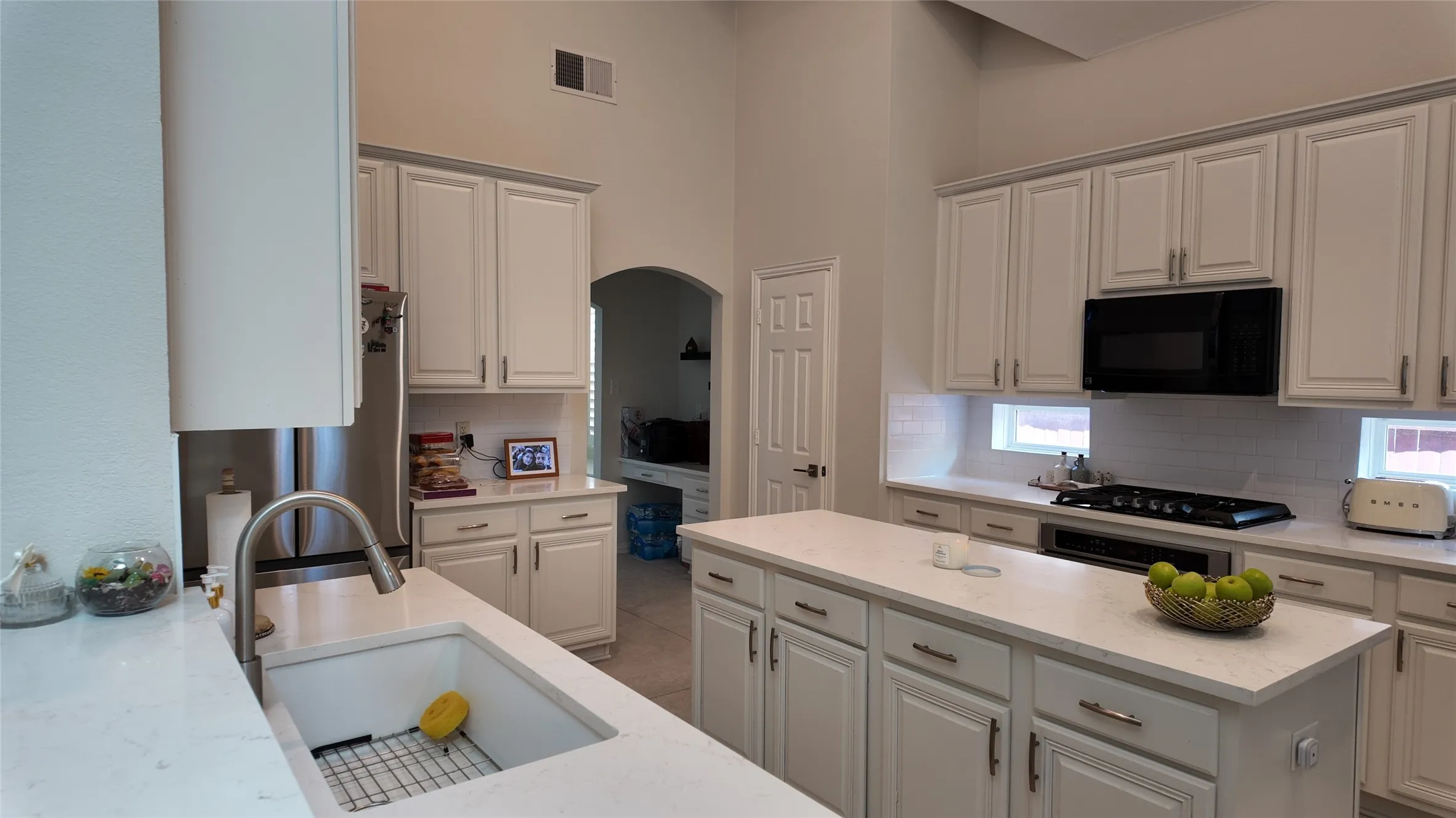 Spacious kitchen featuring an expansive island, white cabinetry, integrated stainless steel sink with gooseneck faucet, sleek black microwave, and coordinating black cooktop