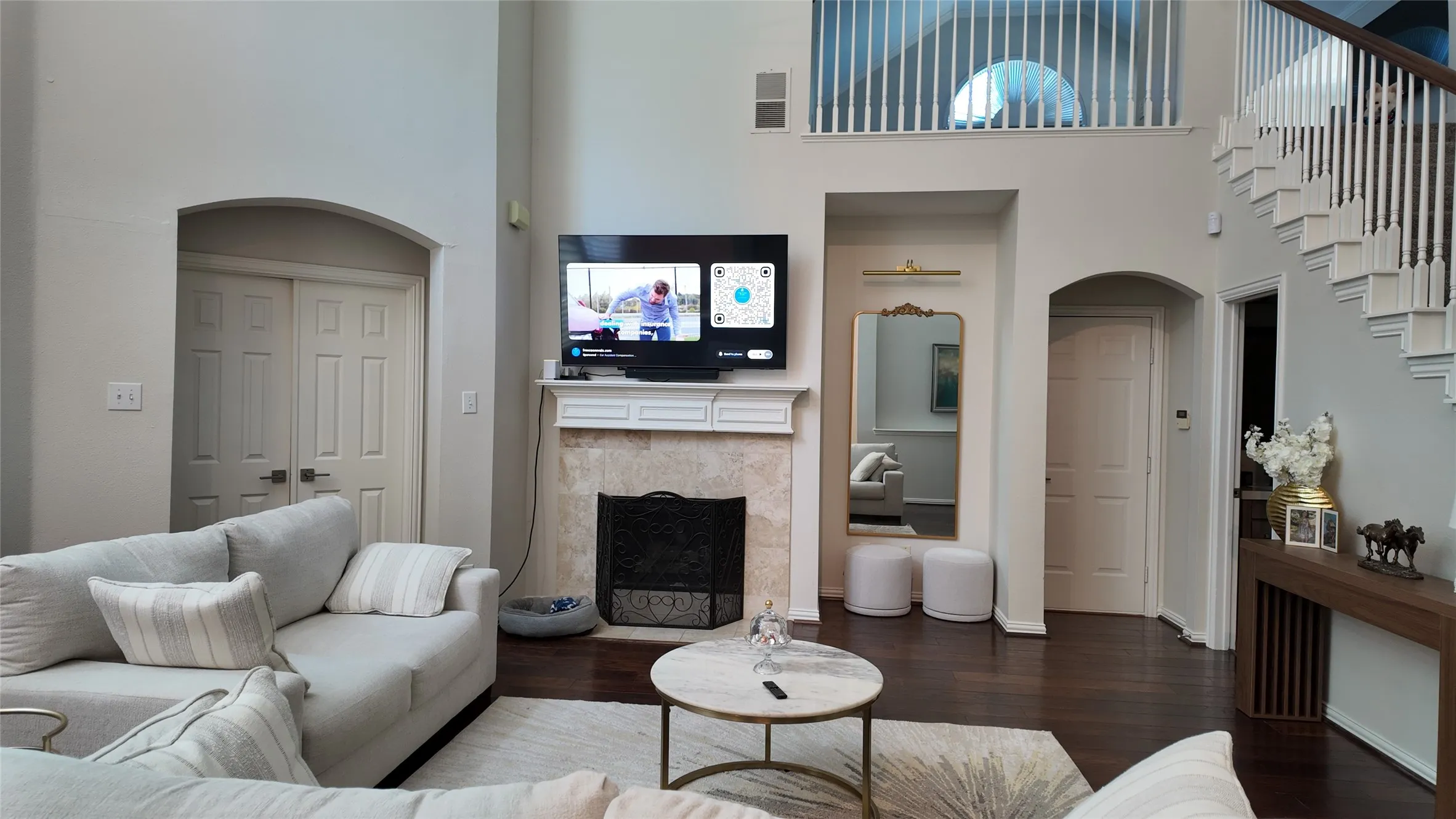 Two-story ceilings, wood-finish flooring, arched doorways, a built-in fireplace with a stone surround, and a white balustrade staircase