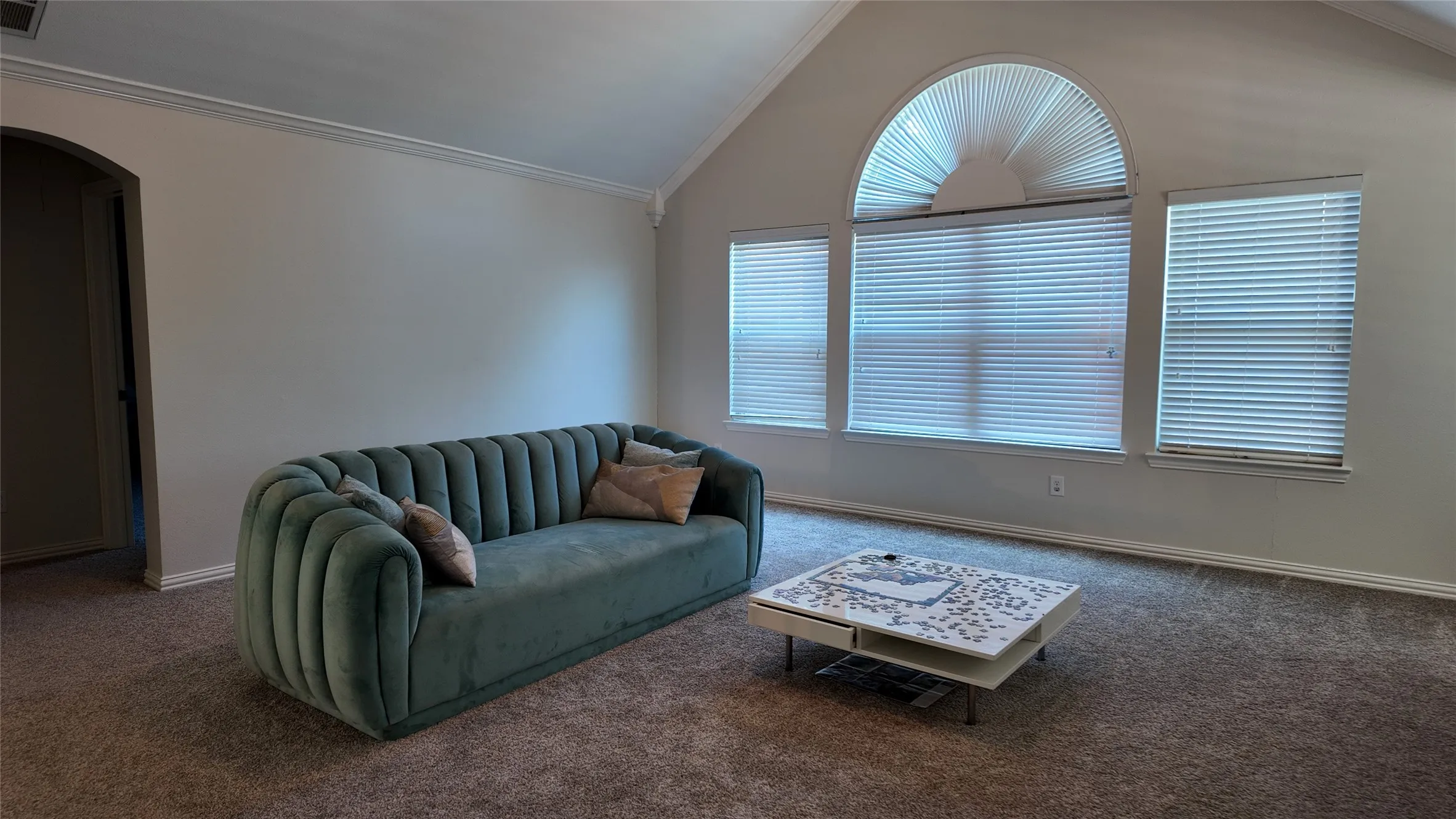 Vaulted ceiling with an arched window, crown molding, and neutral wall tones