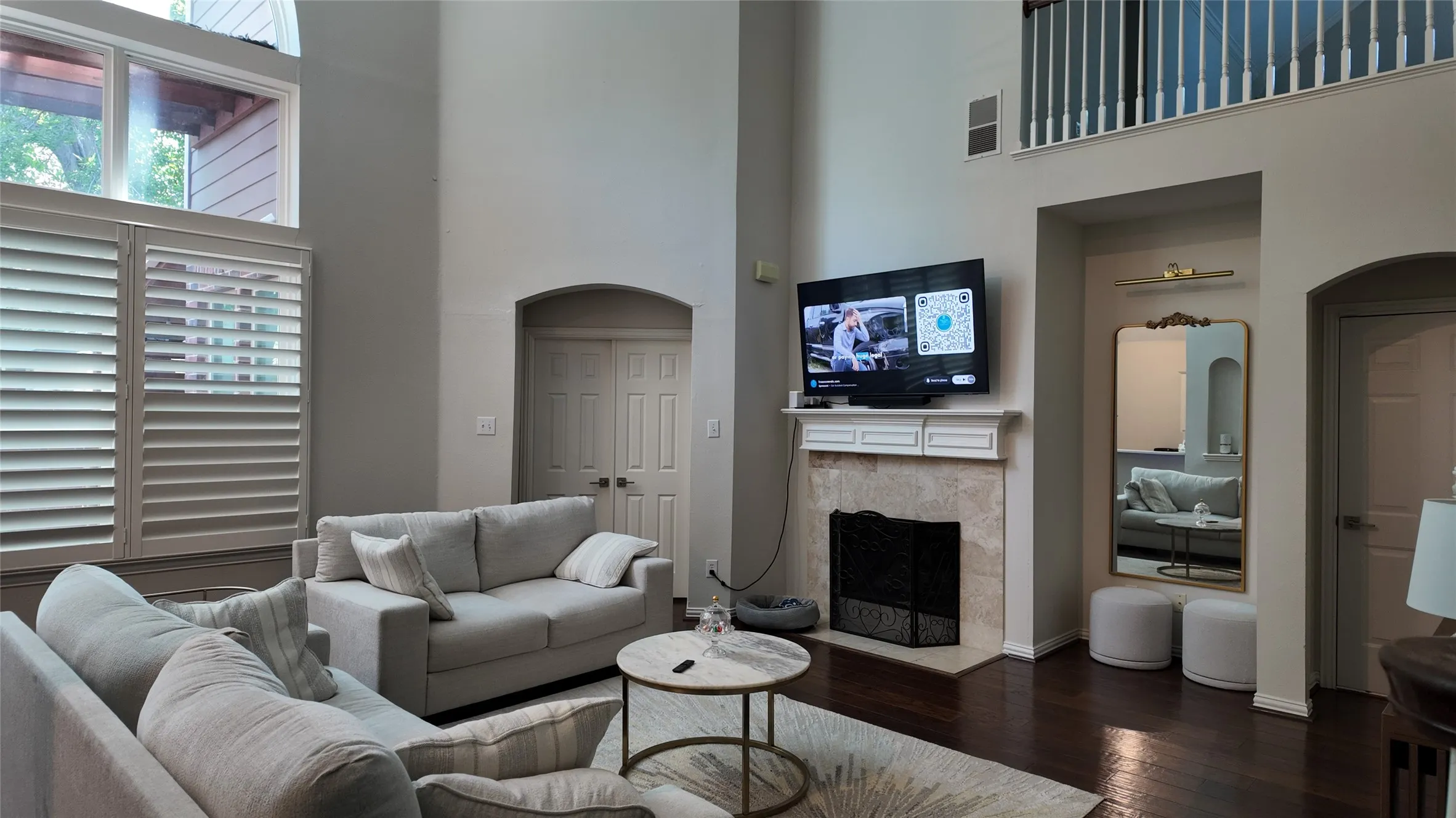 Two-story living area featuring dark wood-finish flooring, a fireplace with a stone surround, and plantation shutters