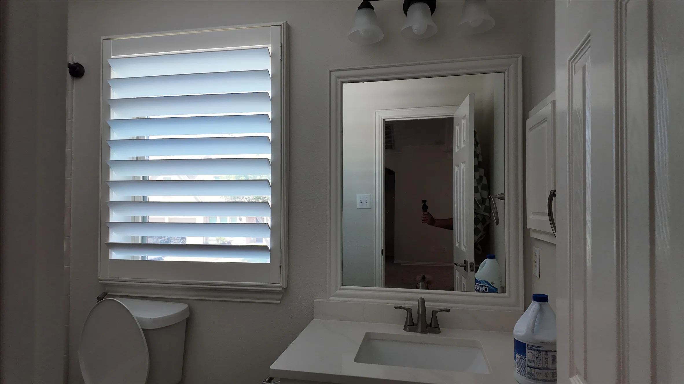 White plantation shutters, vanity with an integrated sink, framed mirror, wall-mounted light fixture, and built-in cabinetry