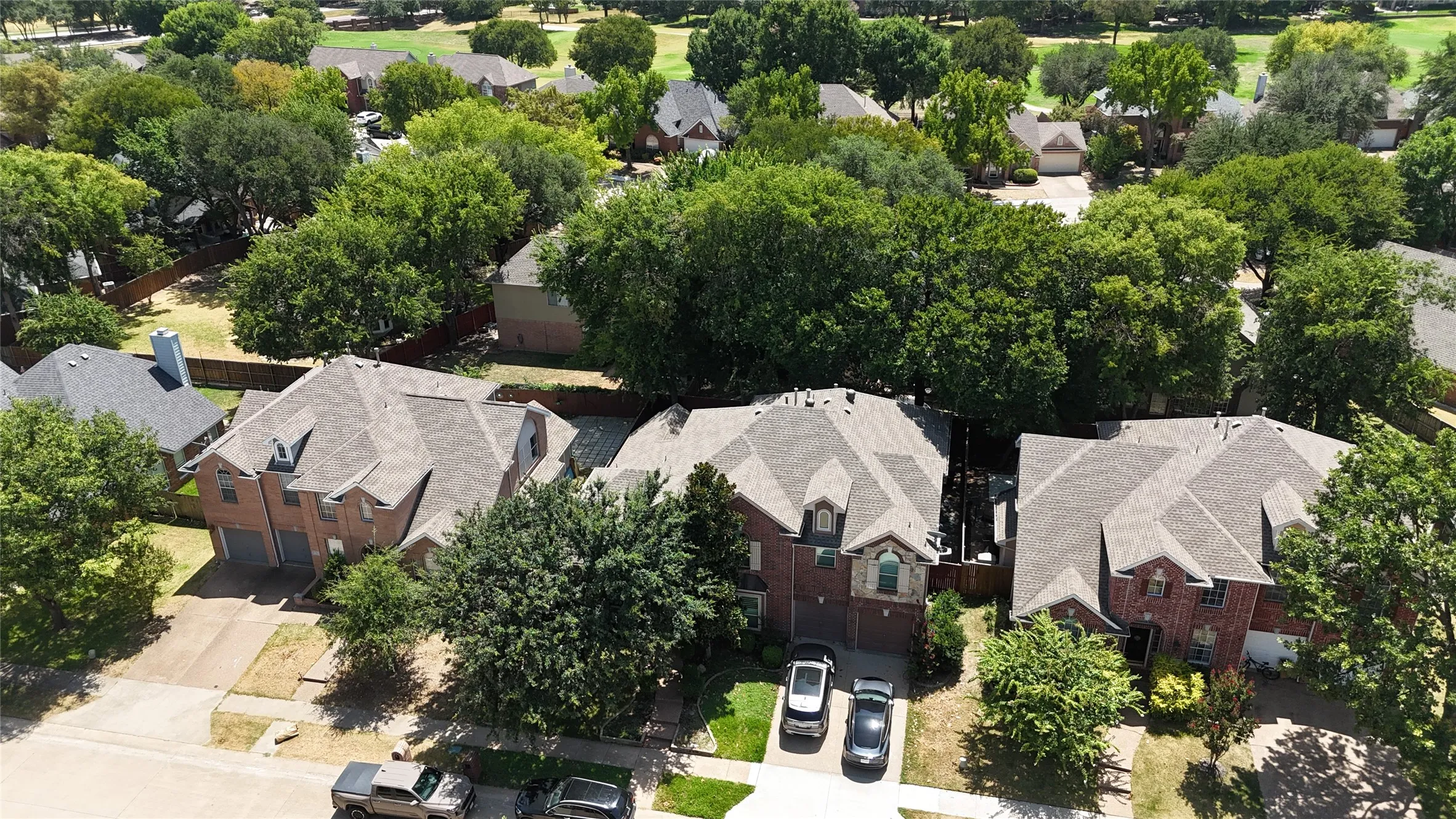 Brick Colonial estate showcasing multiple gabled rooflines with architectural detail, professional landscaping featuring mature trees throughout the grounds, circular driveway with multi-car parking capacity, and expansive manicured lawn with established perimeter landscaping
